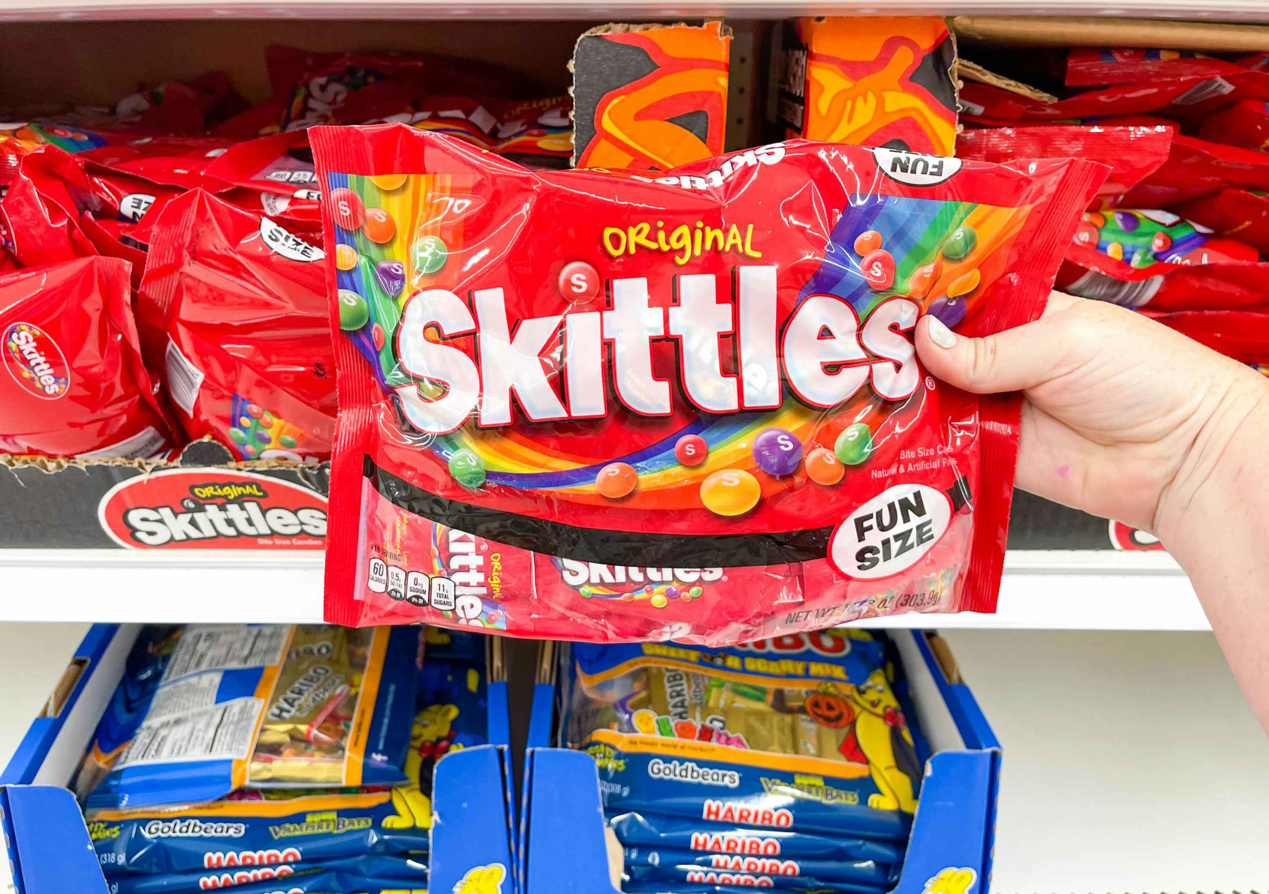 a person holding skittles in store by cart