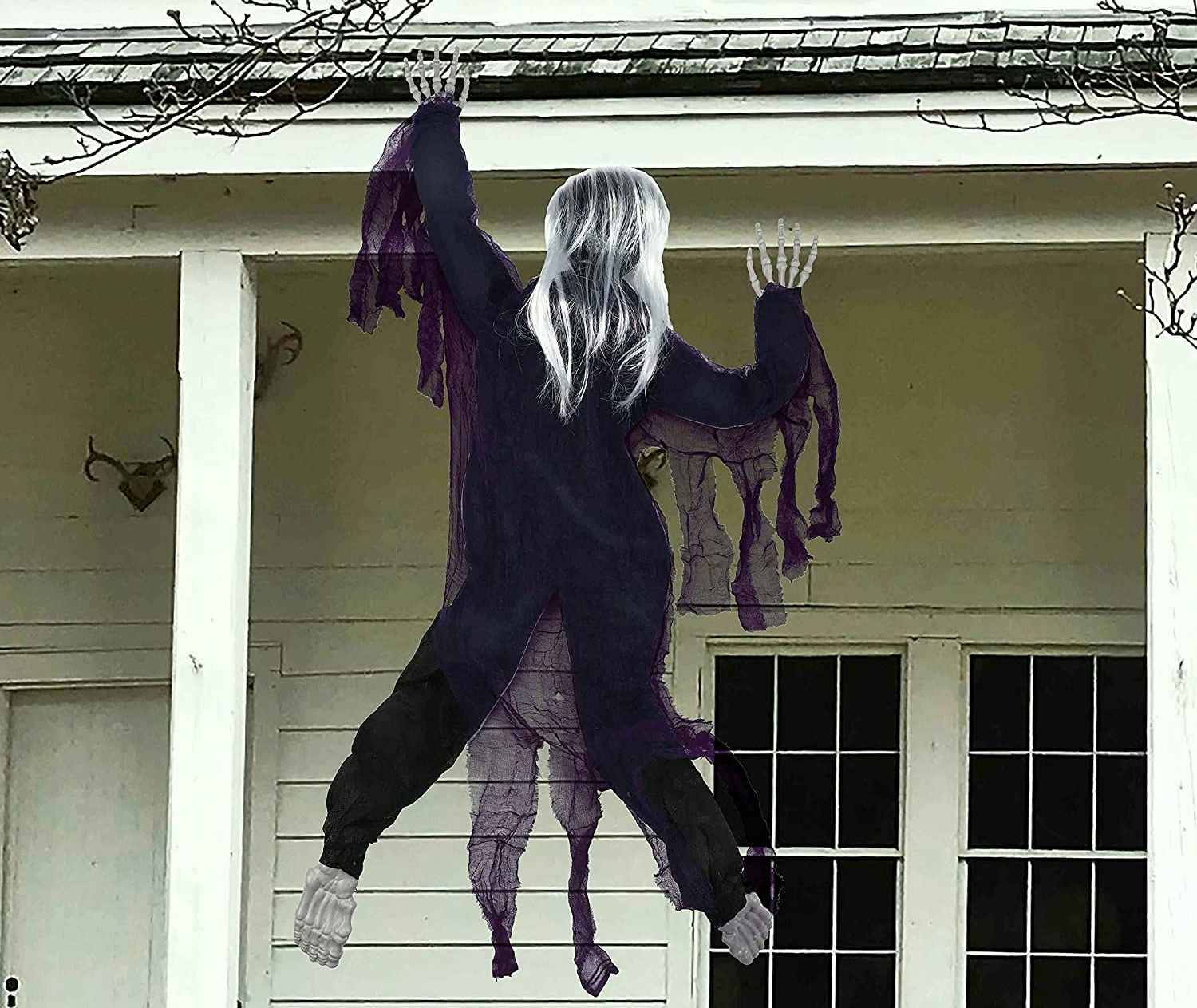 A zombie decoration hanging off the roof of a house.