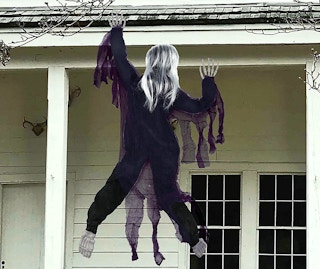 A zombie decoration hanging off the roof of a house.