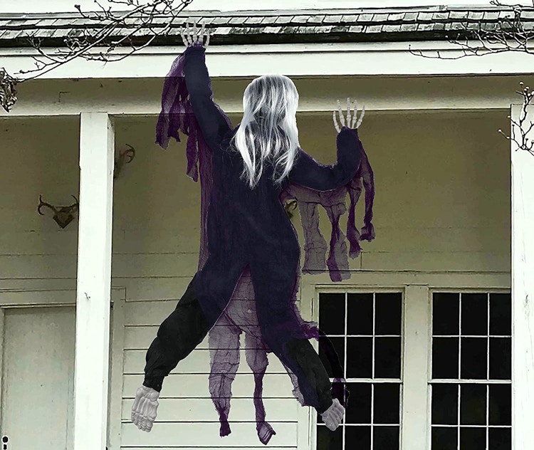 A zombie decoration hanging off the roof of a house.