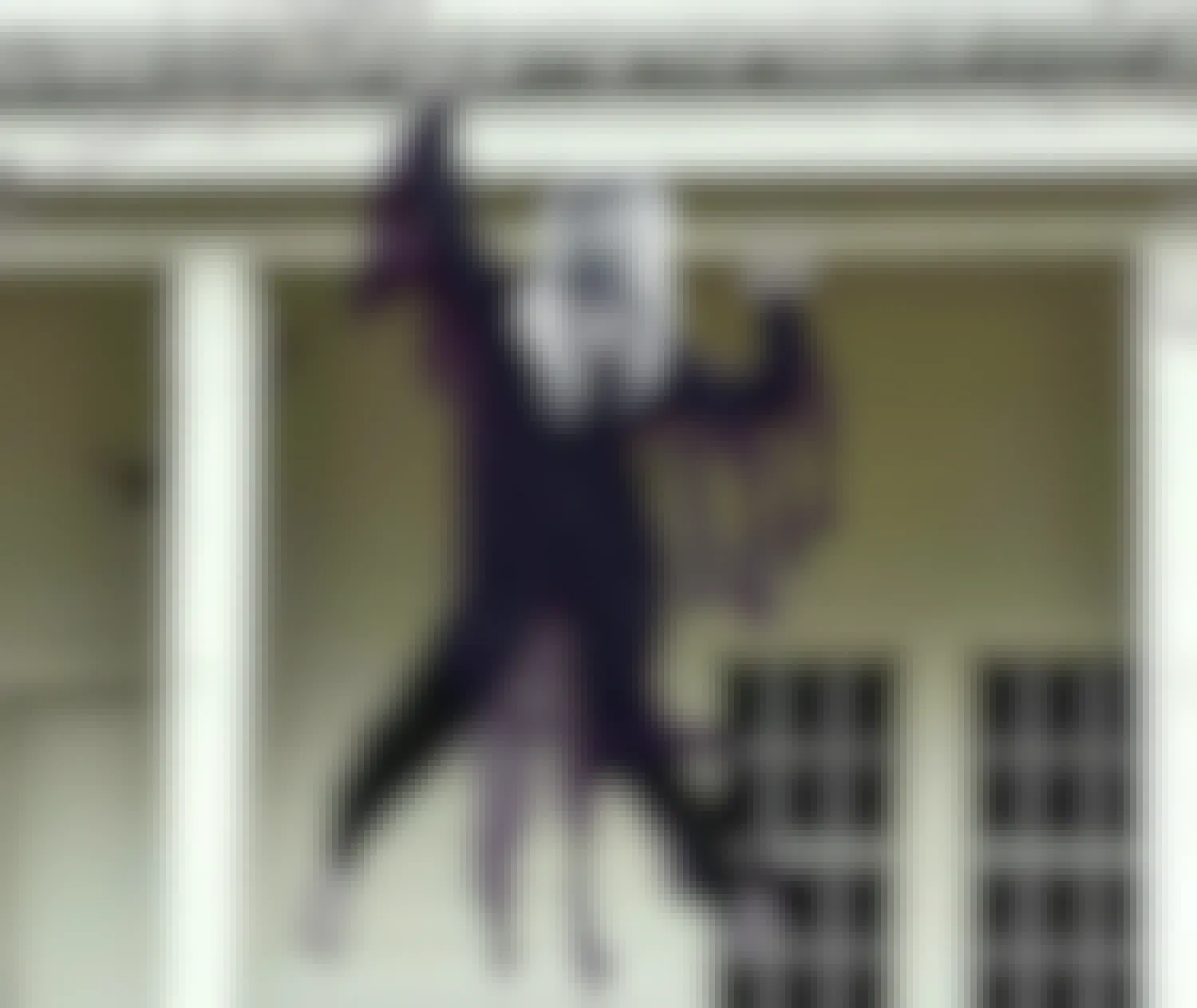 A zombie decoration hanging off the roof of a house.