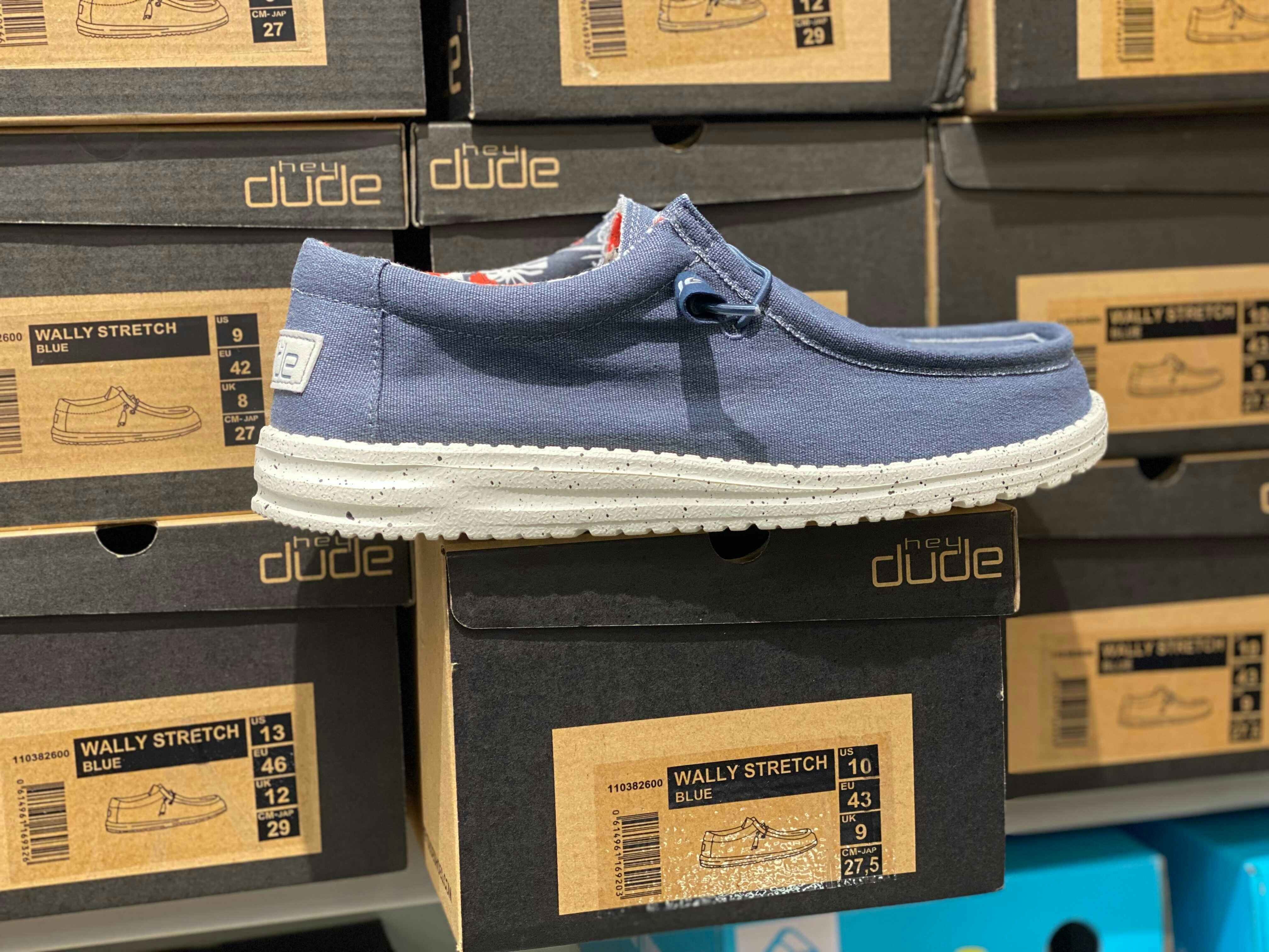 A dark blue Hey Dude shoe in front of a stack of shoe boxes in a store.