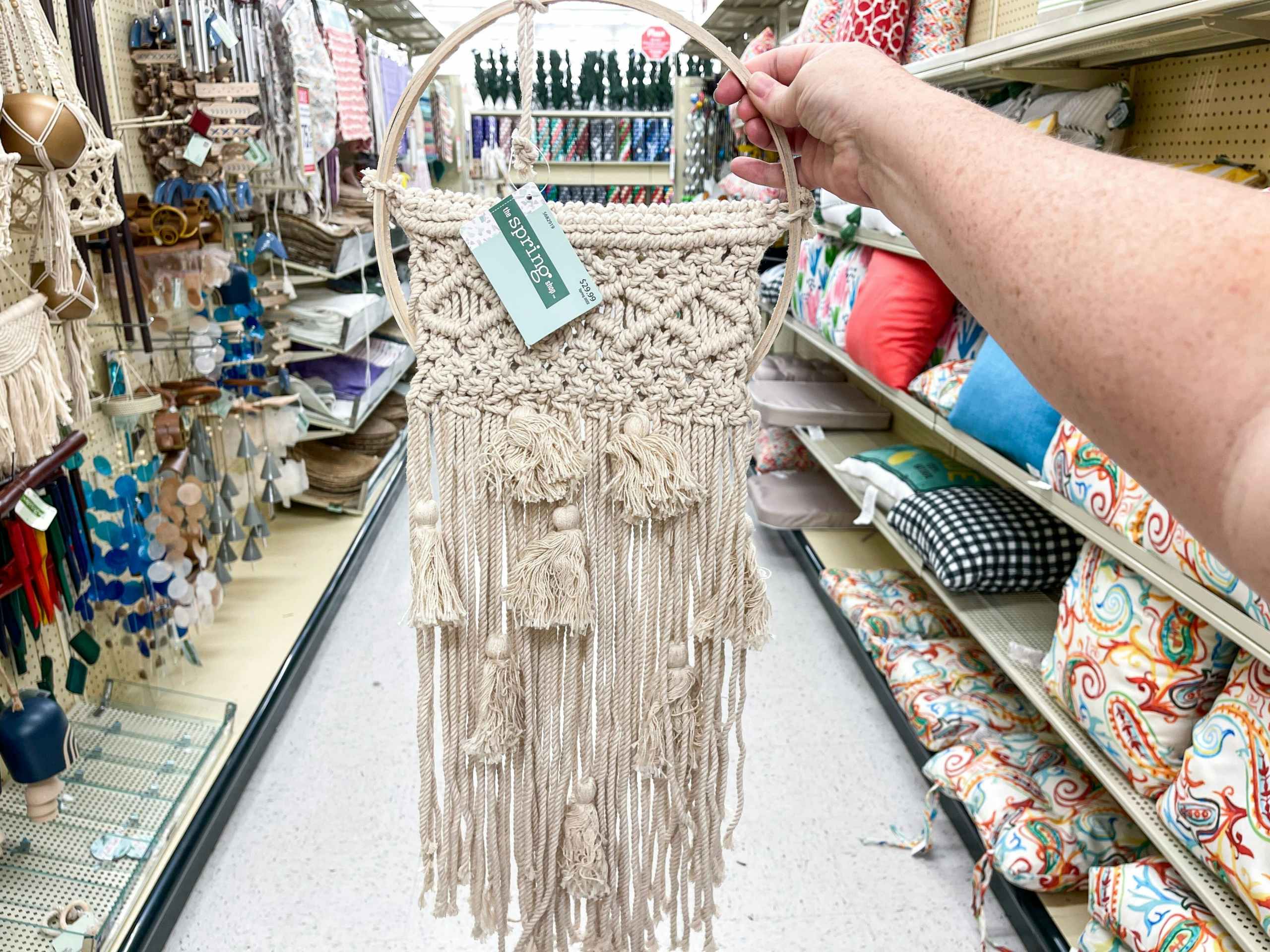 someone holding up macrame wall decor in an aisle