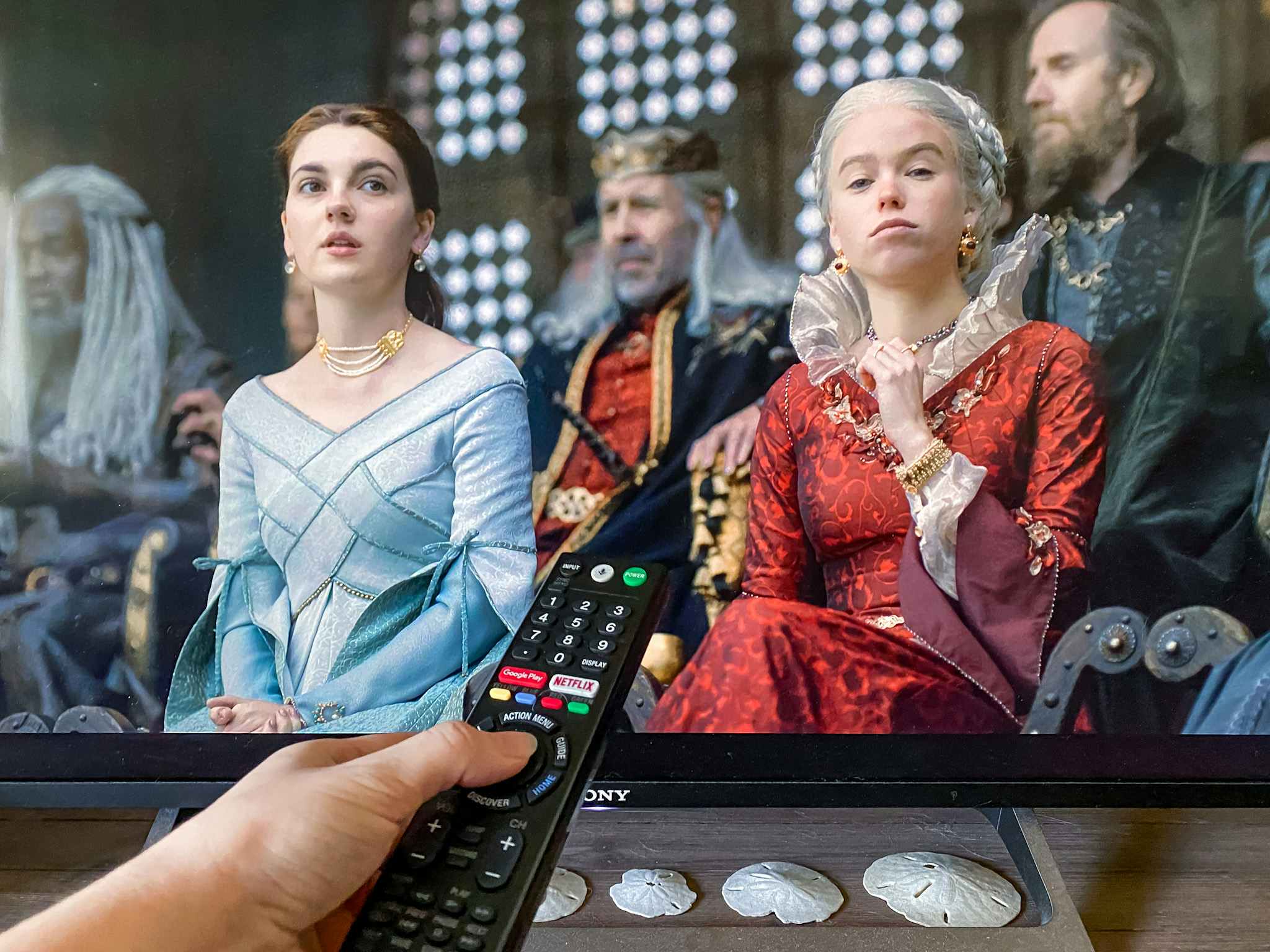 A person's hand pointing a remote at a TV playing the first episode of House of the Dragon on HBO.