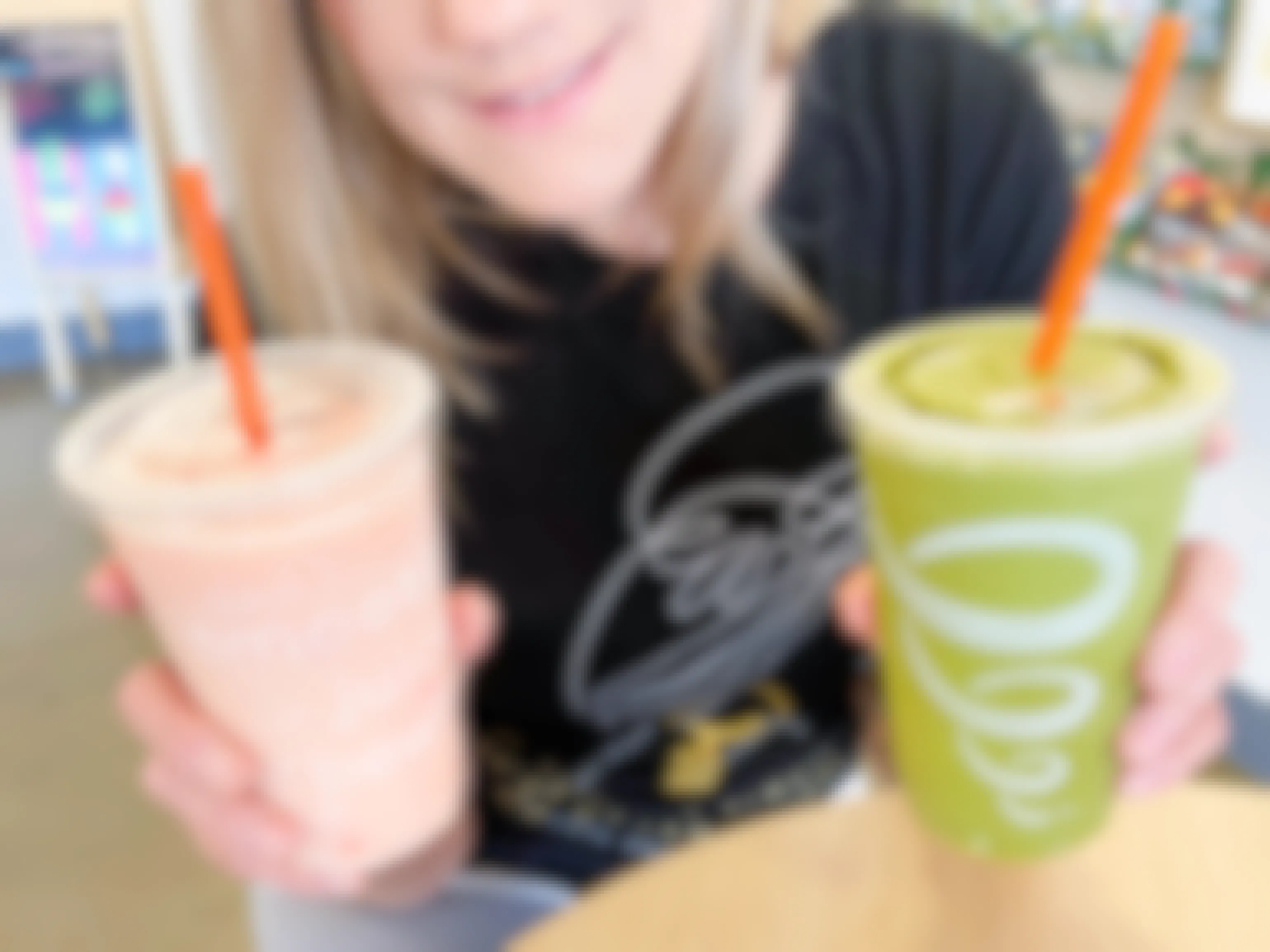 woman holding two smoothies on table