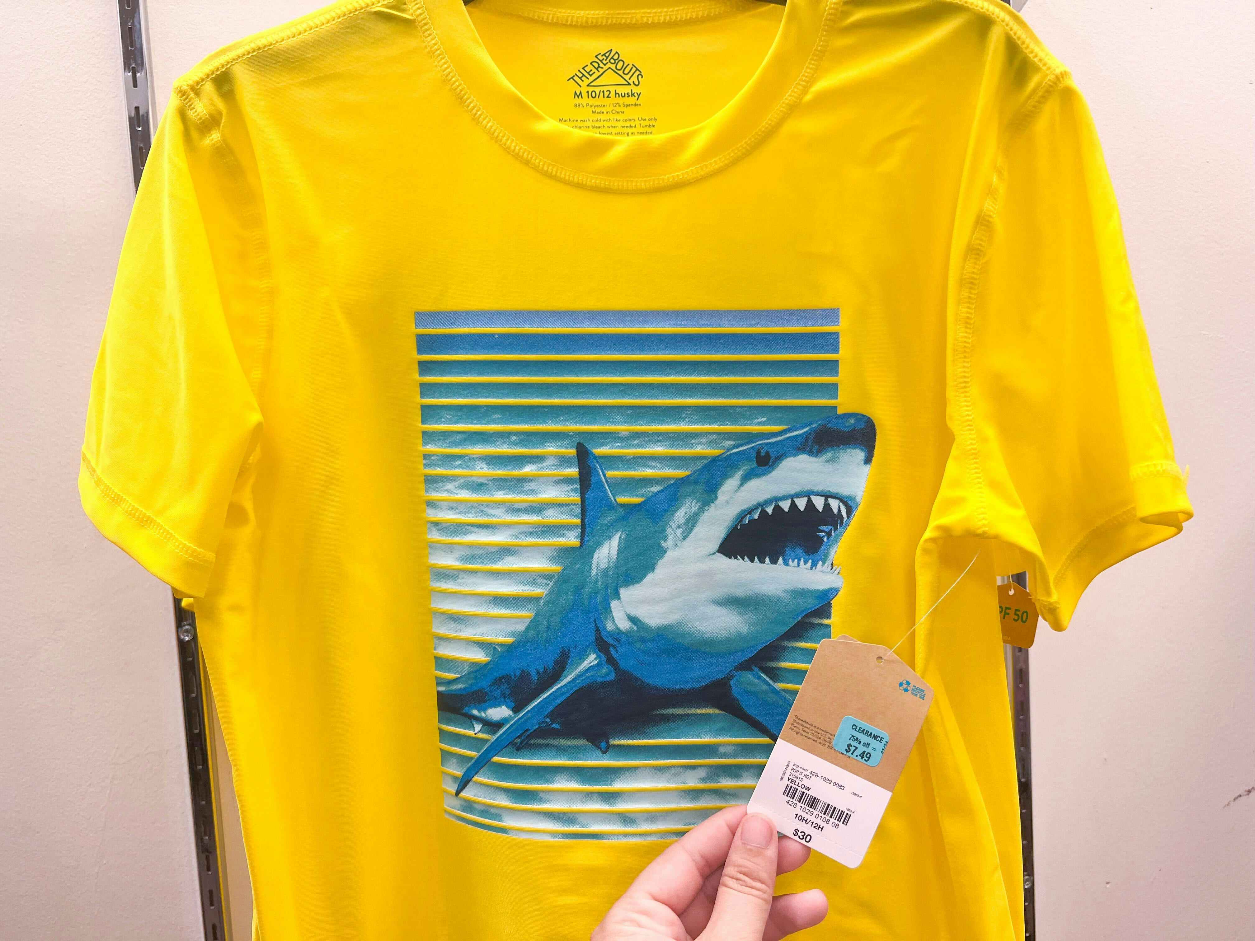someone holding the tag to a kids yellow shirt with a shark on it