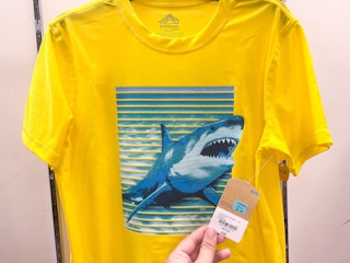 someone holding the tag to a kids yellow shirt with a shark on it