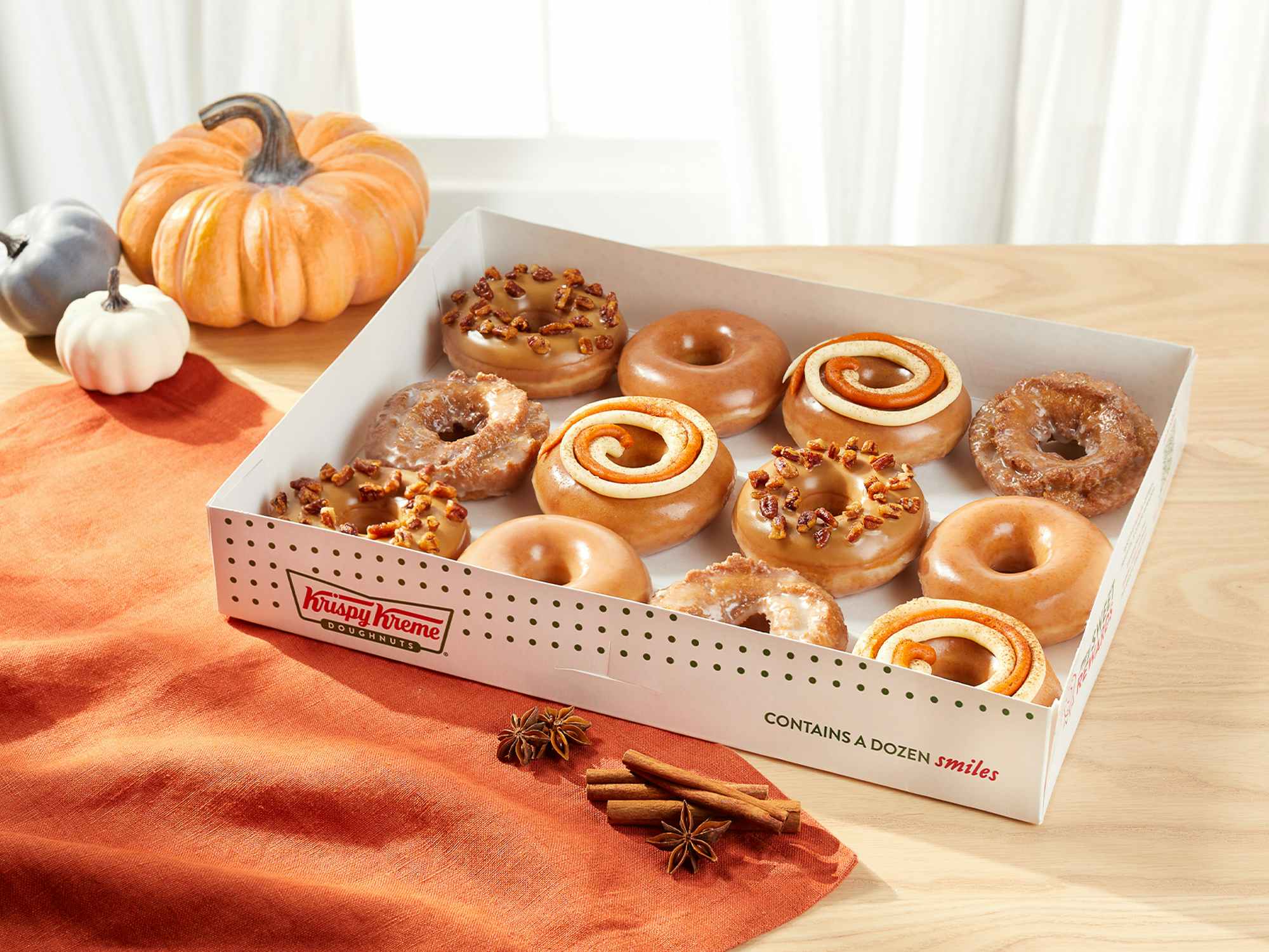 a box of pumpkin spice Krispy Kreme doughnuts on a table next to fall decor