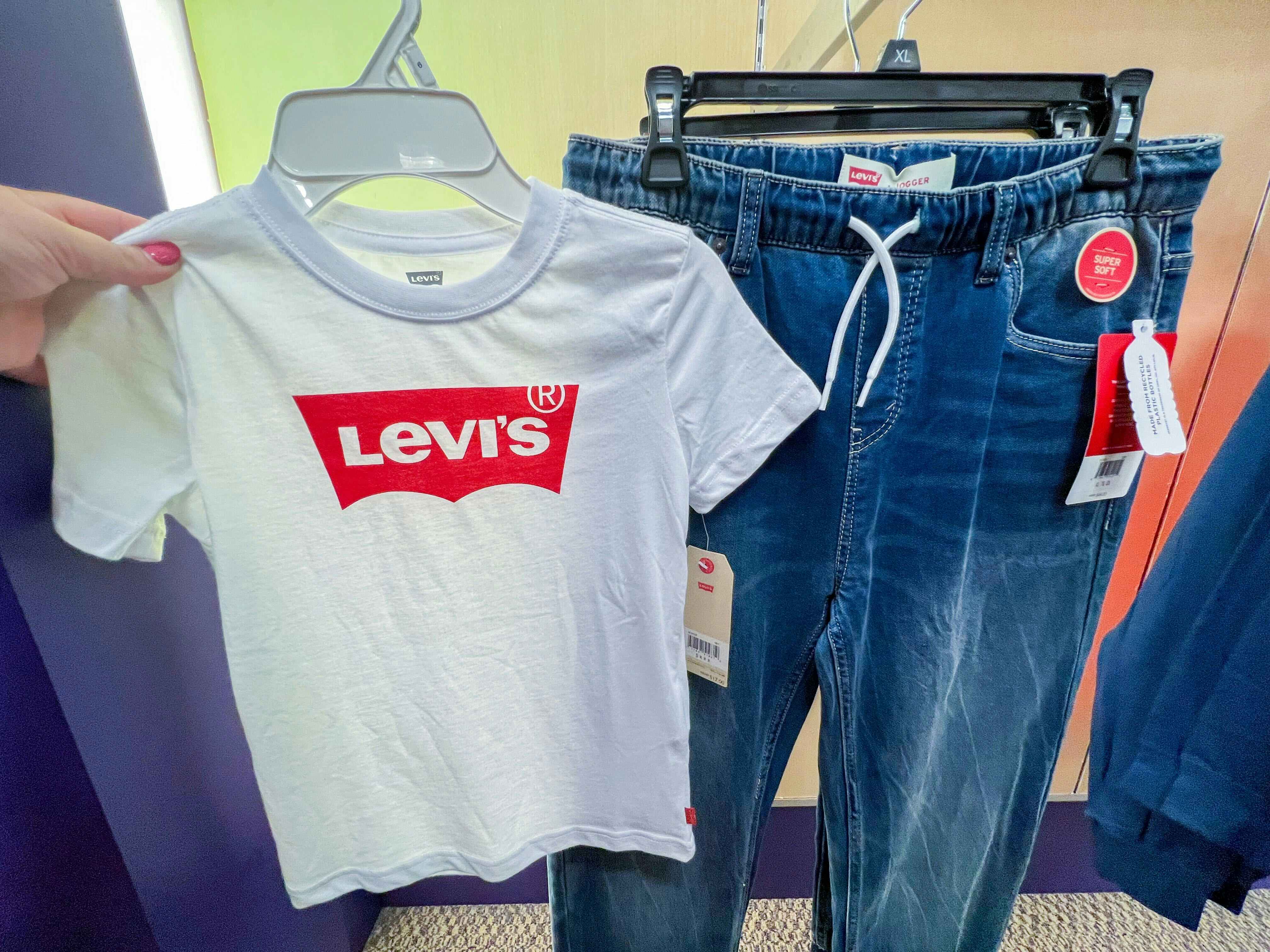 A hand holding a white Levi Shirt, with a pair of Levi jeans