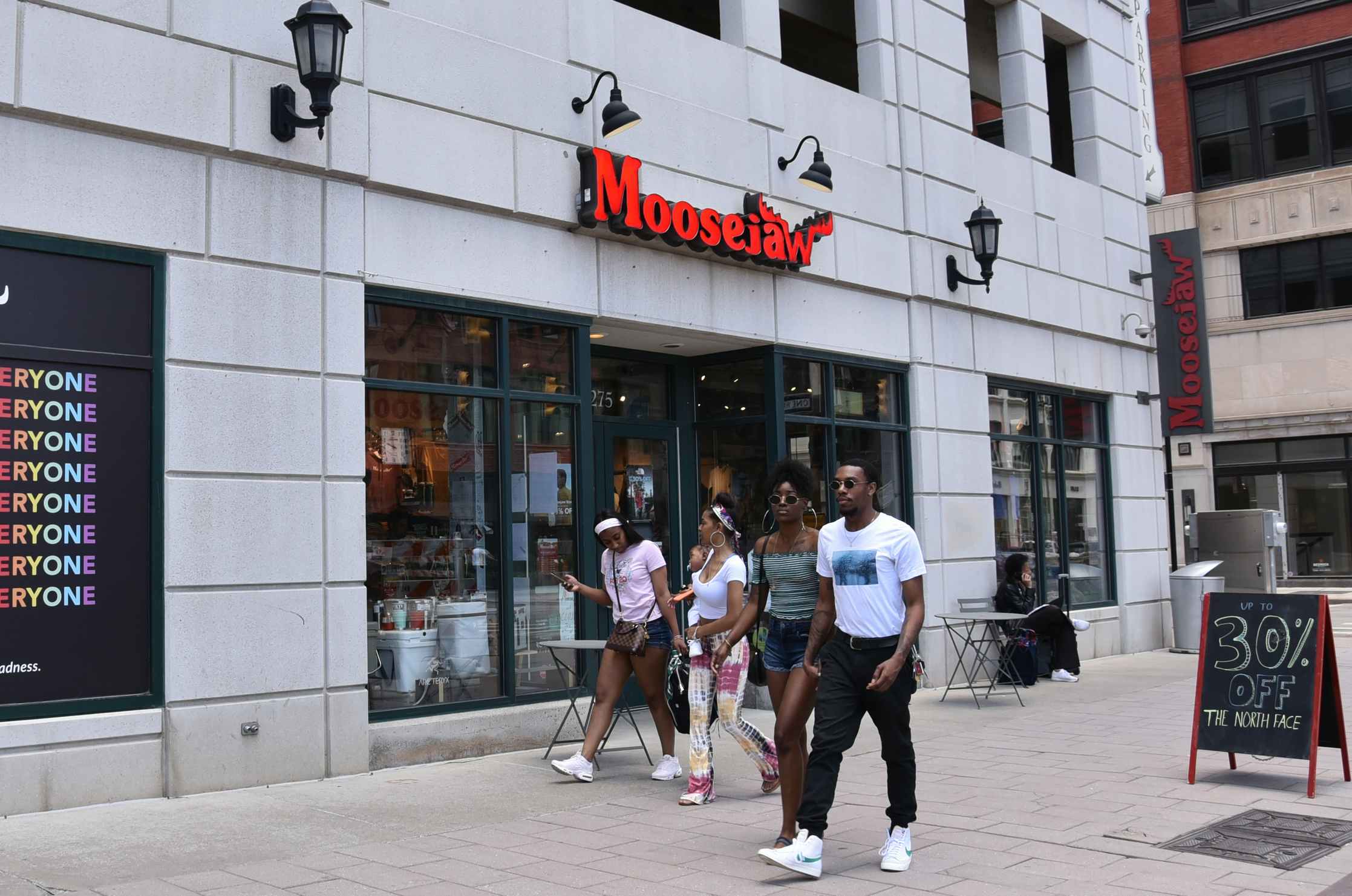 people walking by a moosejaw storefront in the city