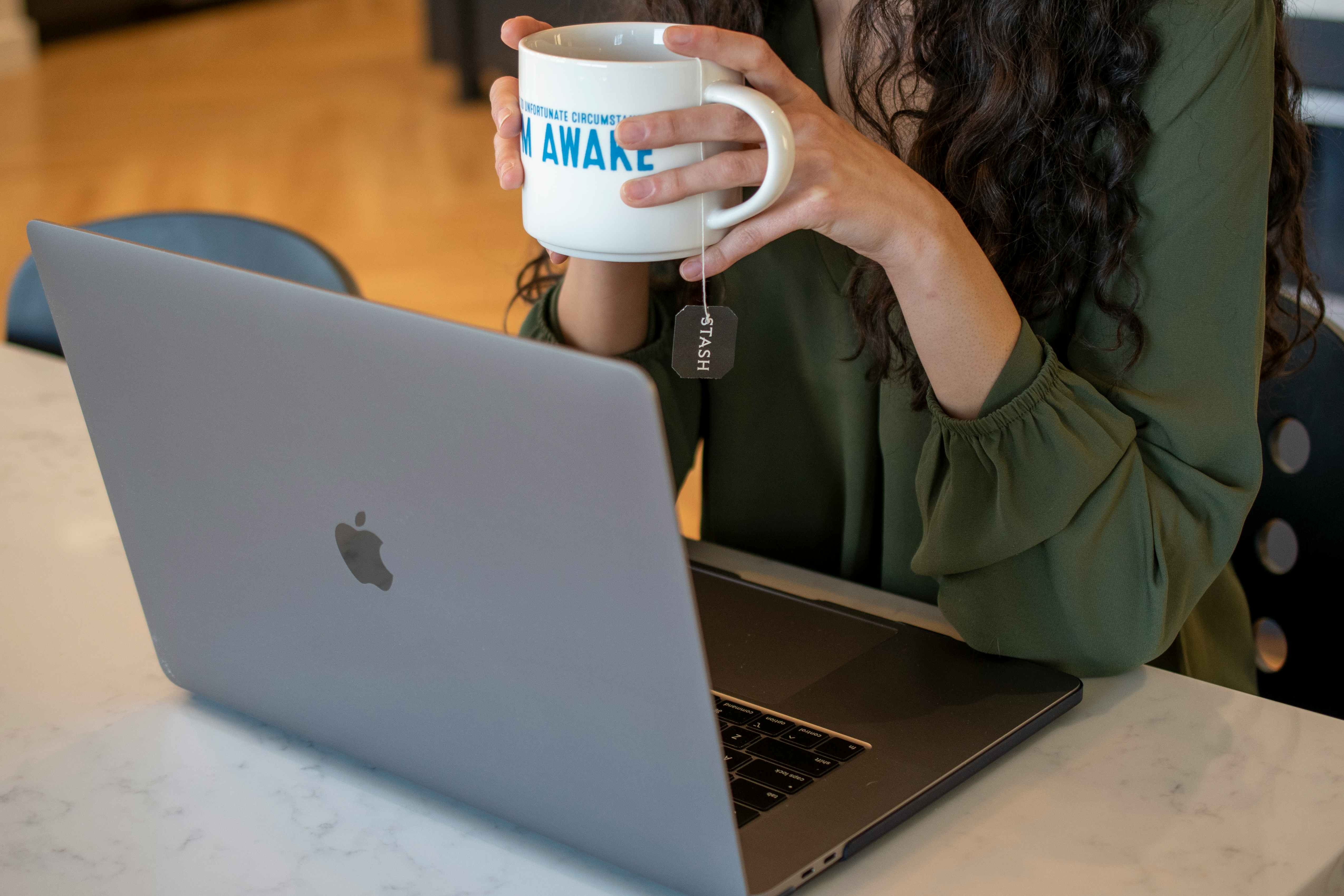 A person holding a mug looking at a laptop computer.