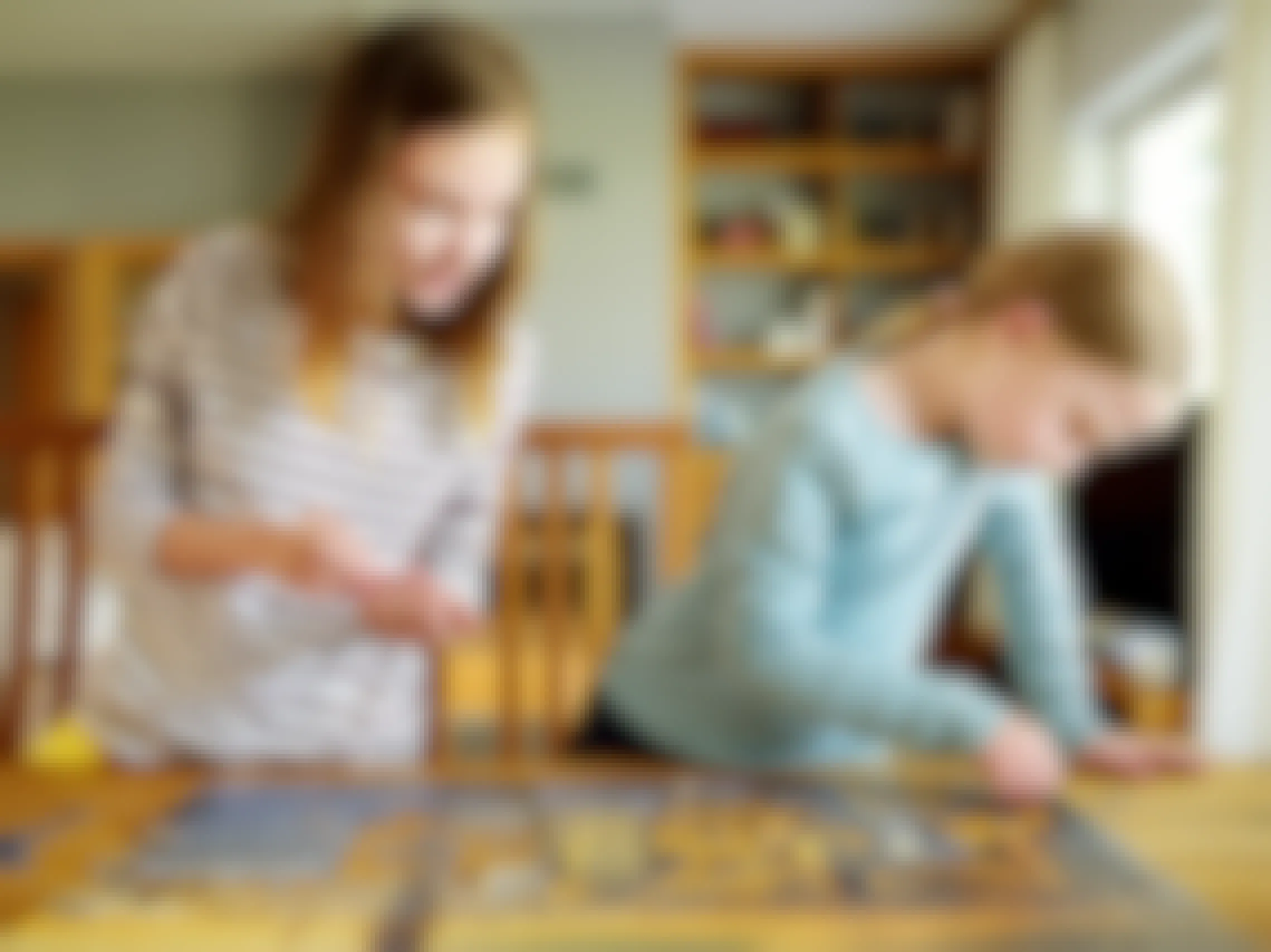 Two girls working on a jigsaw puzzle on a wooden table in their house.