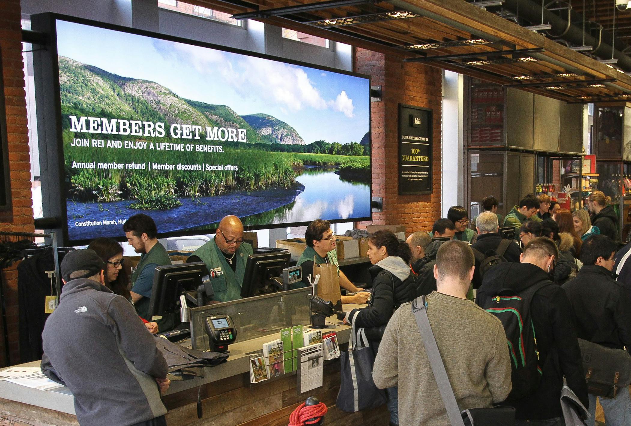 customers in REI store checkout line with member sign