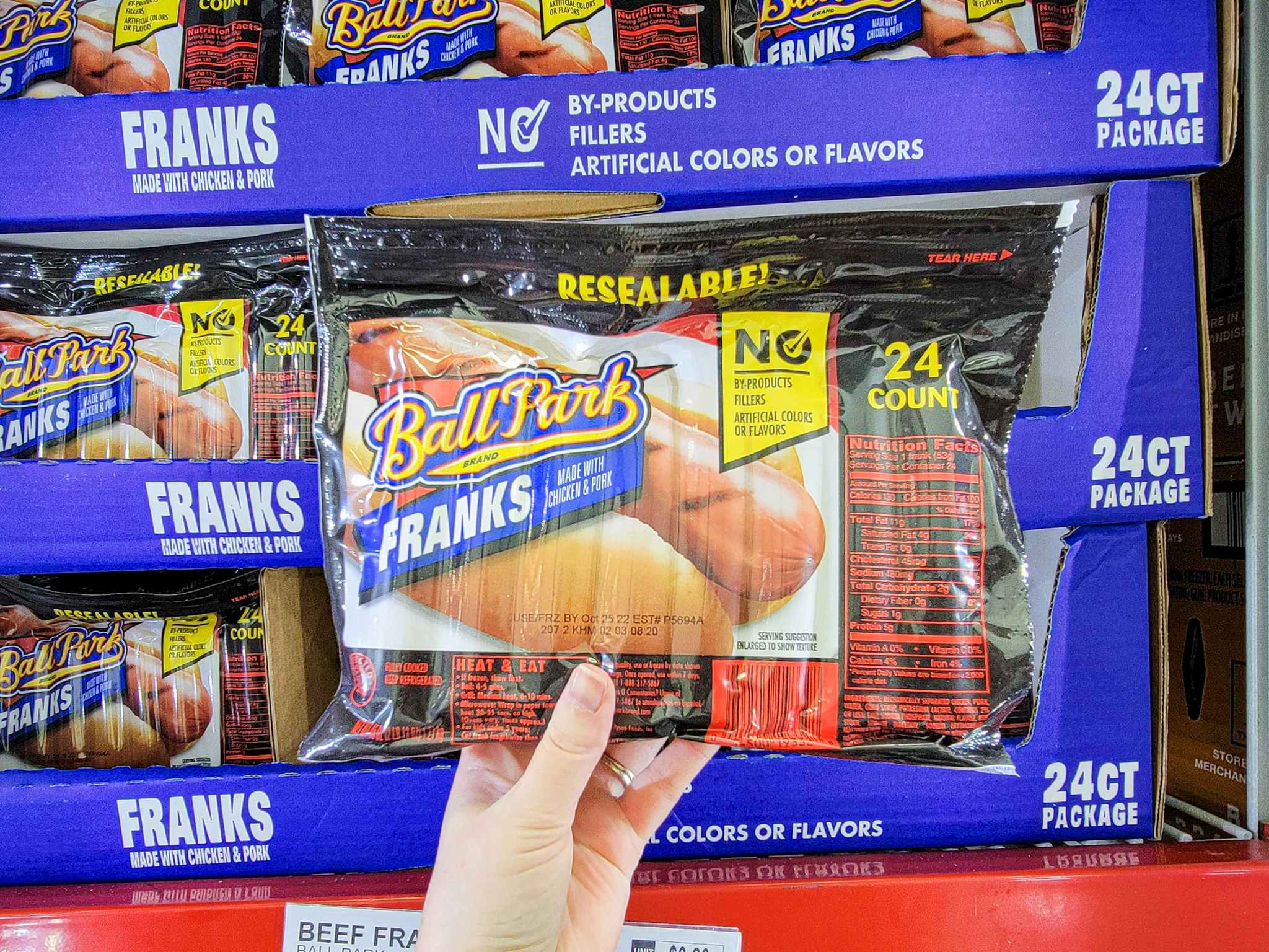 hand holding a pack of 24 ball park hot dogs