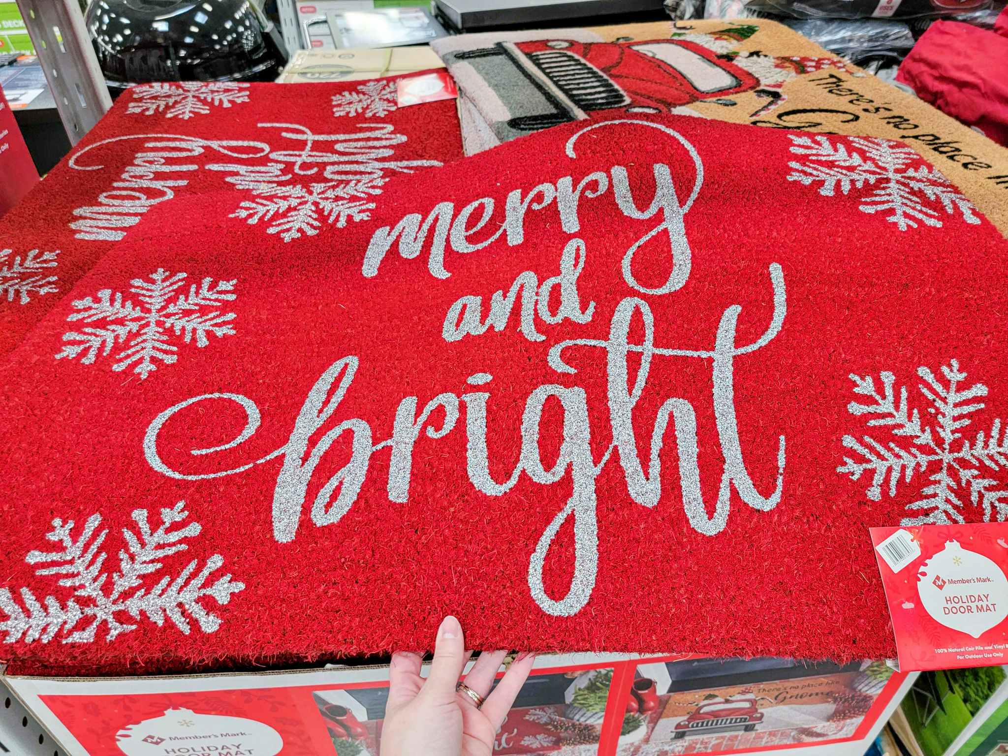 hand holding a red door mat that says merry & bright