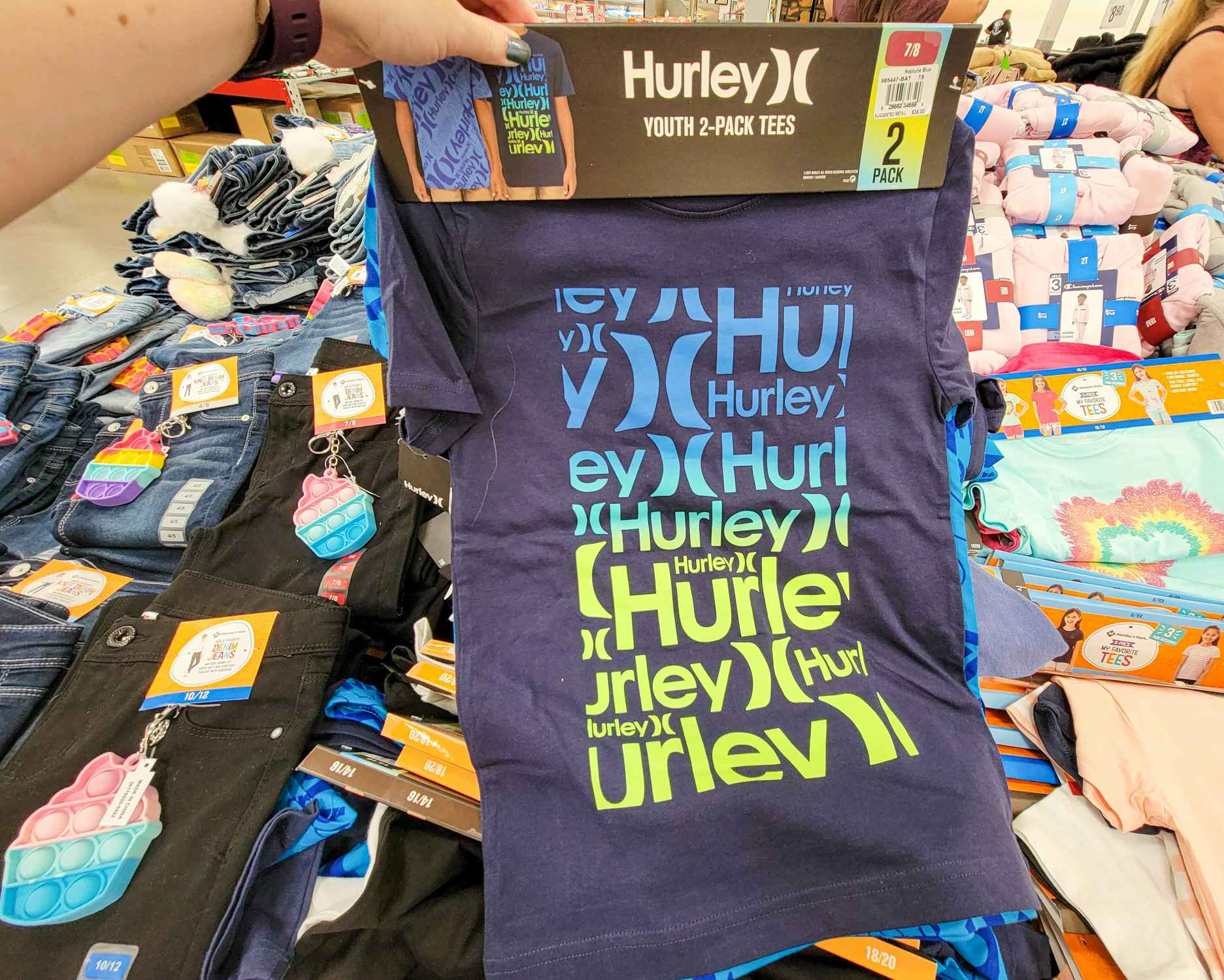 hand holding a 2 pack of kids hurley shirts, front one is navy blue with hurley written numerous times in yellow and blue