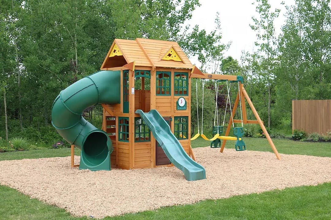 a large swingset set up in a backyard with a tube slide, regular slide, swings, and clubhouse