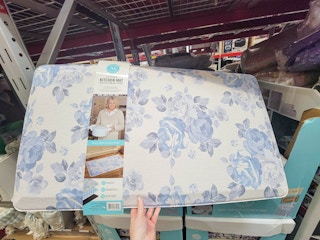 hand holding an anti fatigue kitchen mat, white with blue floral design