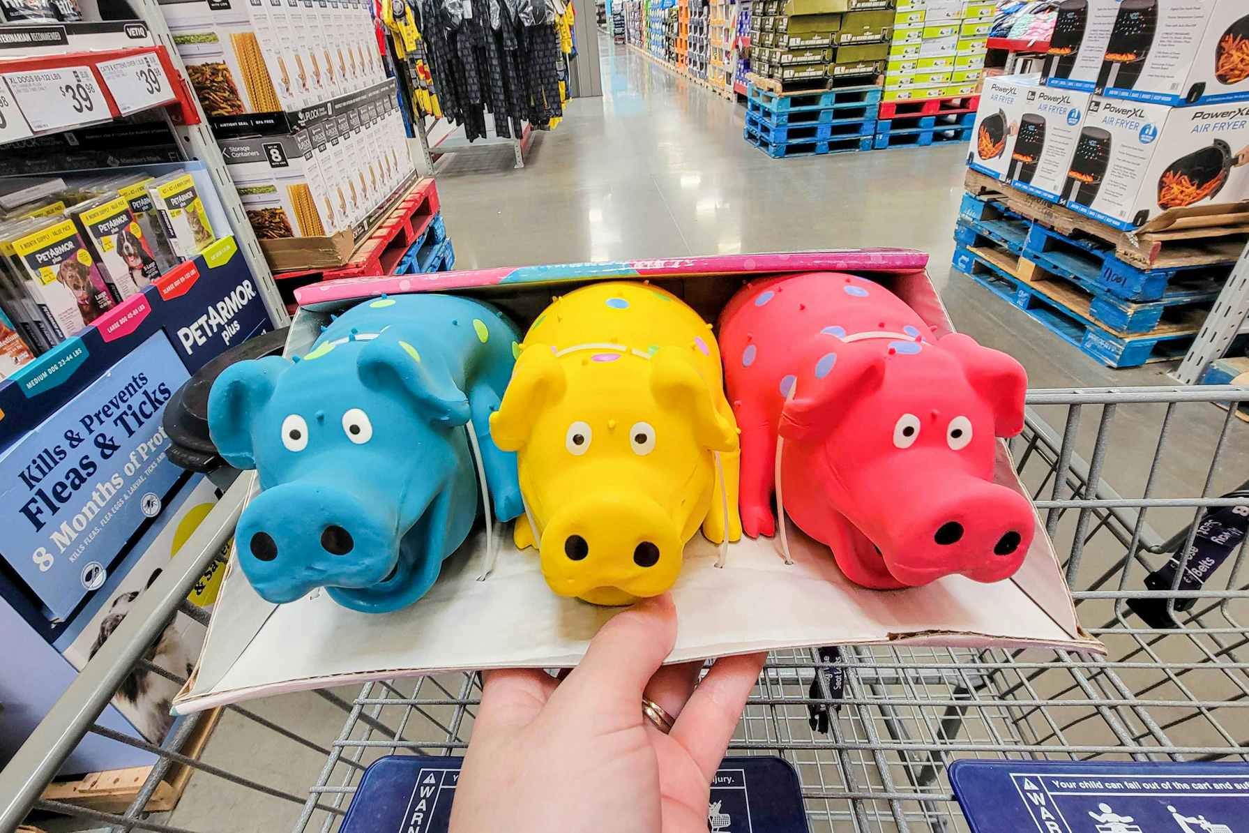 hand holding a 3-pack of multipet polka dot pig dog toys over a cart
