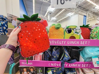 hand holding a strawberry lunch bag by a pineapple and avocado lunch bag