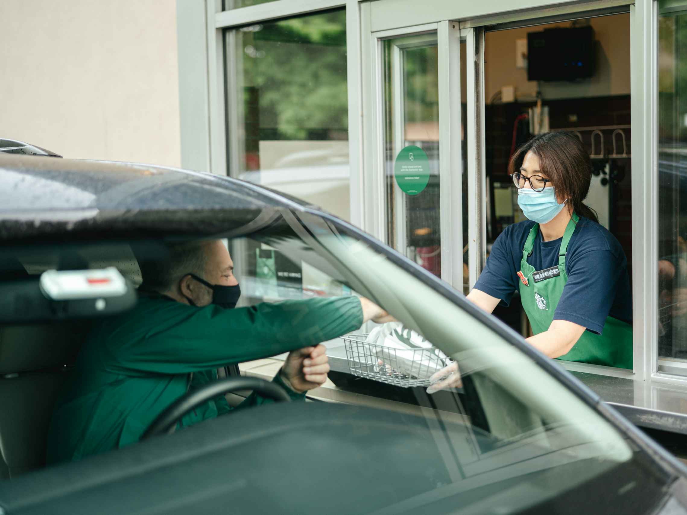 A man in his car taking food from a Starbucks barista at the drive through window.