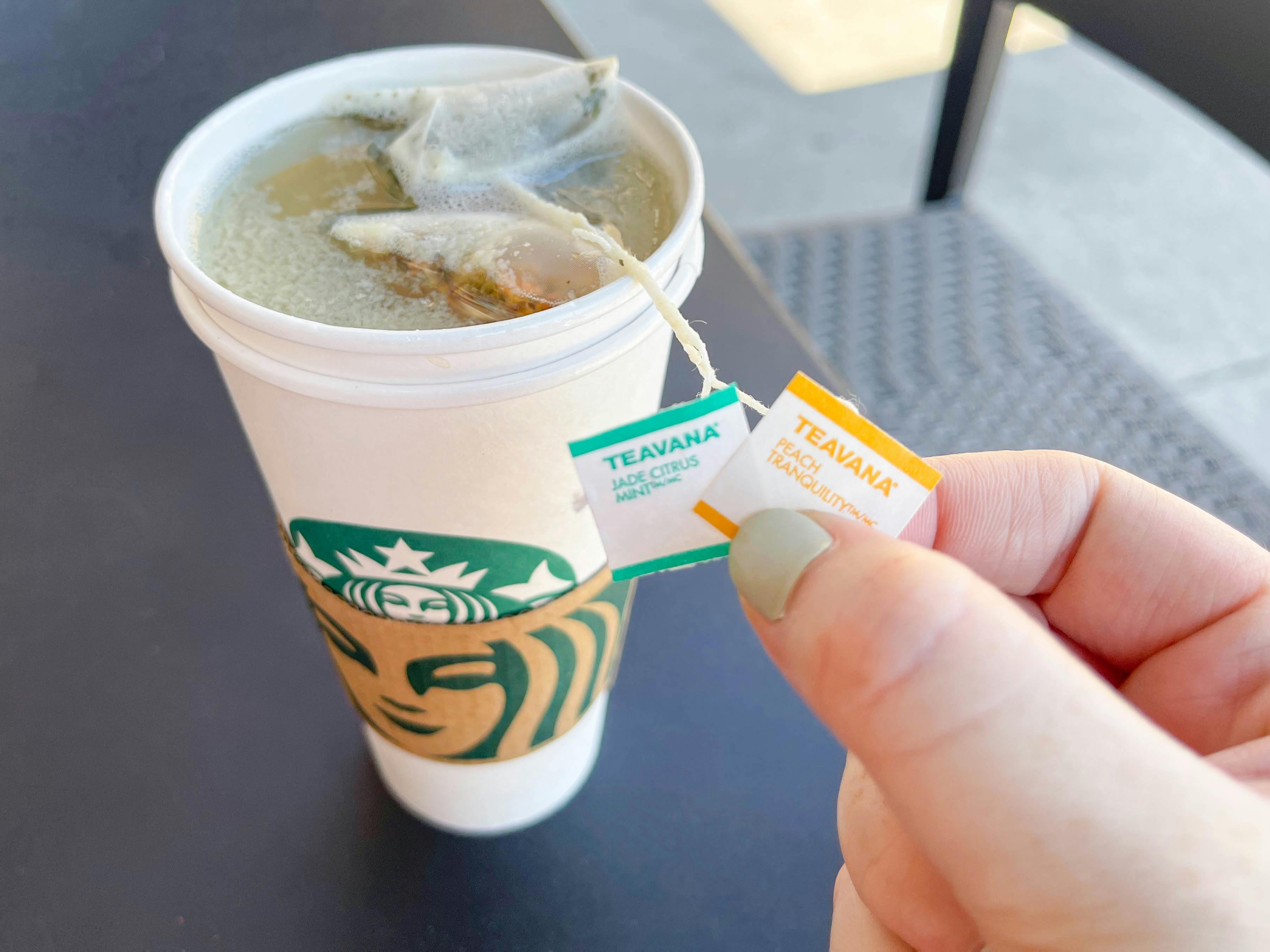 A Starbucks tea sitting on a table with the tea bags labels being held up.