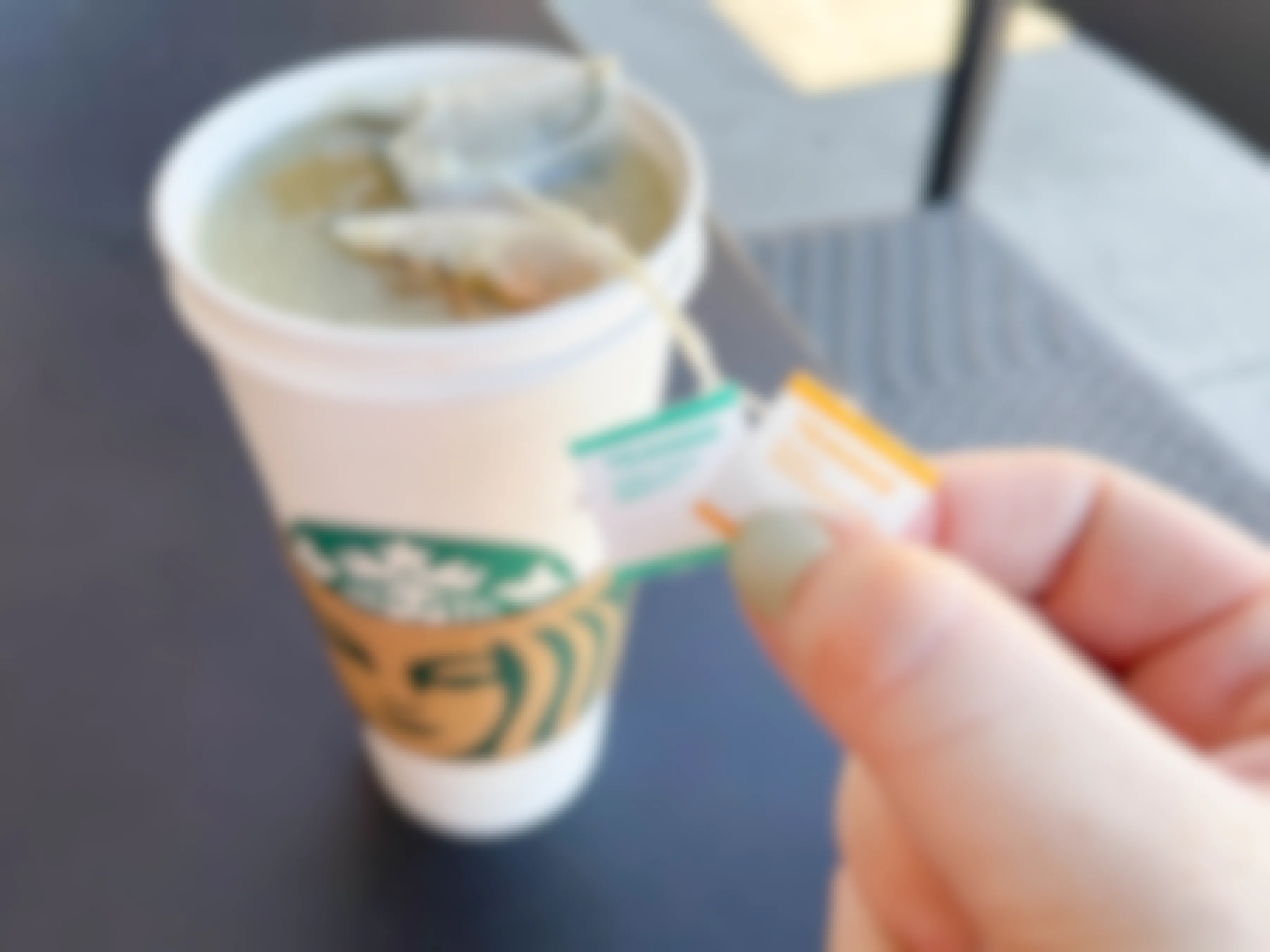 A Starbucks tea sitting on a table with the tea bags labels being held up.