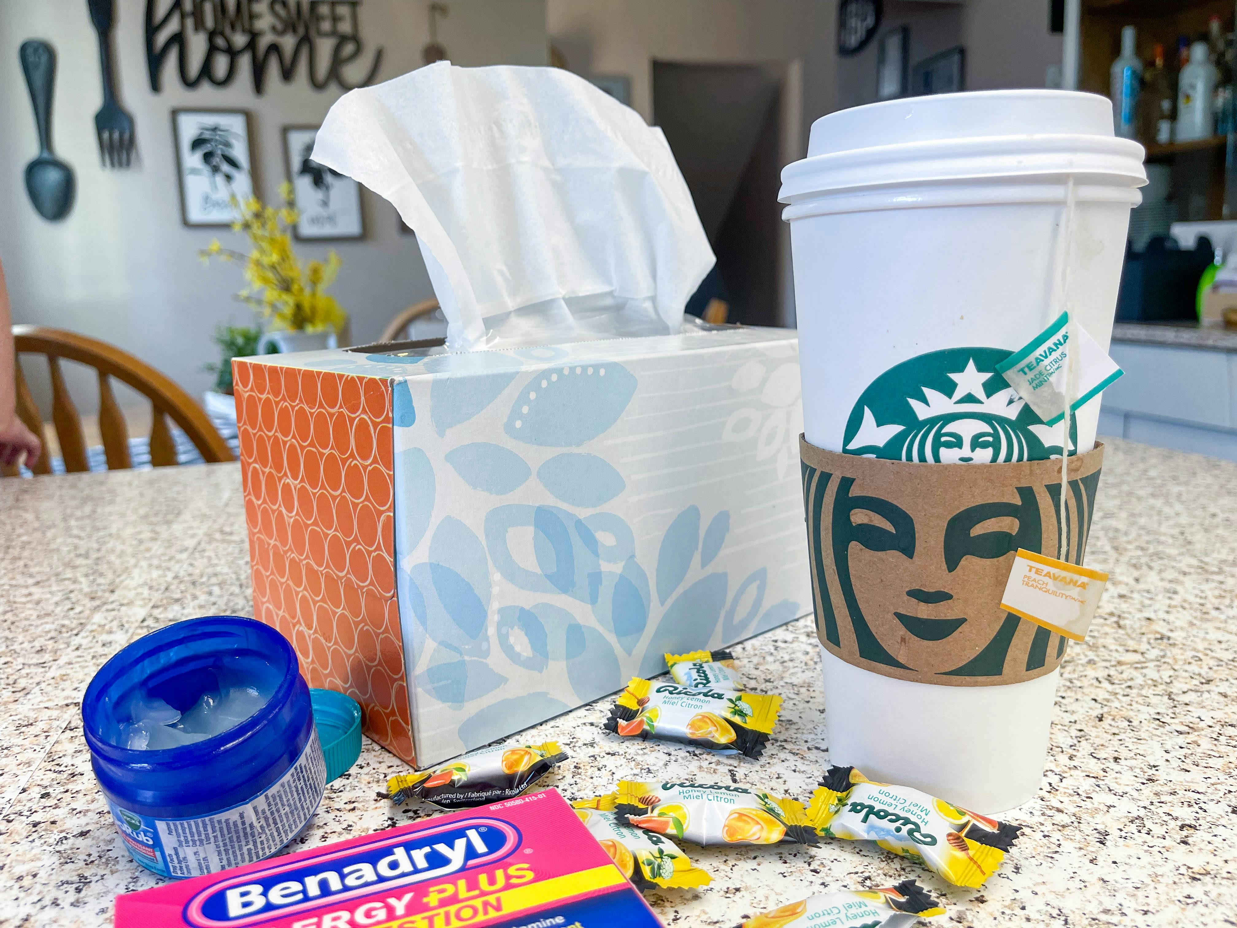 A Starbucks tea on a counter near a box of cold medicine and tissues.