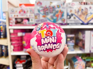 A 5 Surprise Toy Mini Brands being held in front of a Target toy shelf