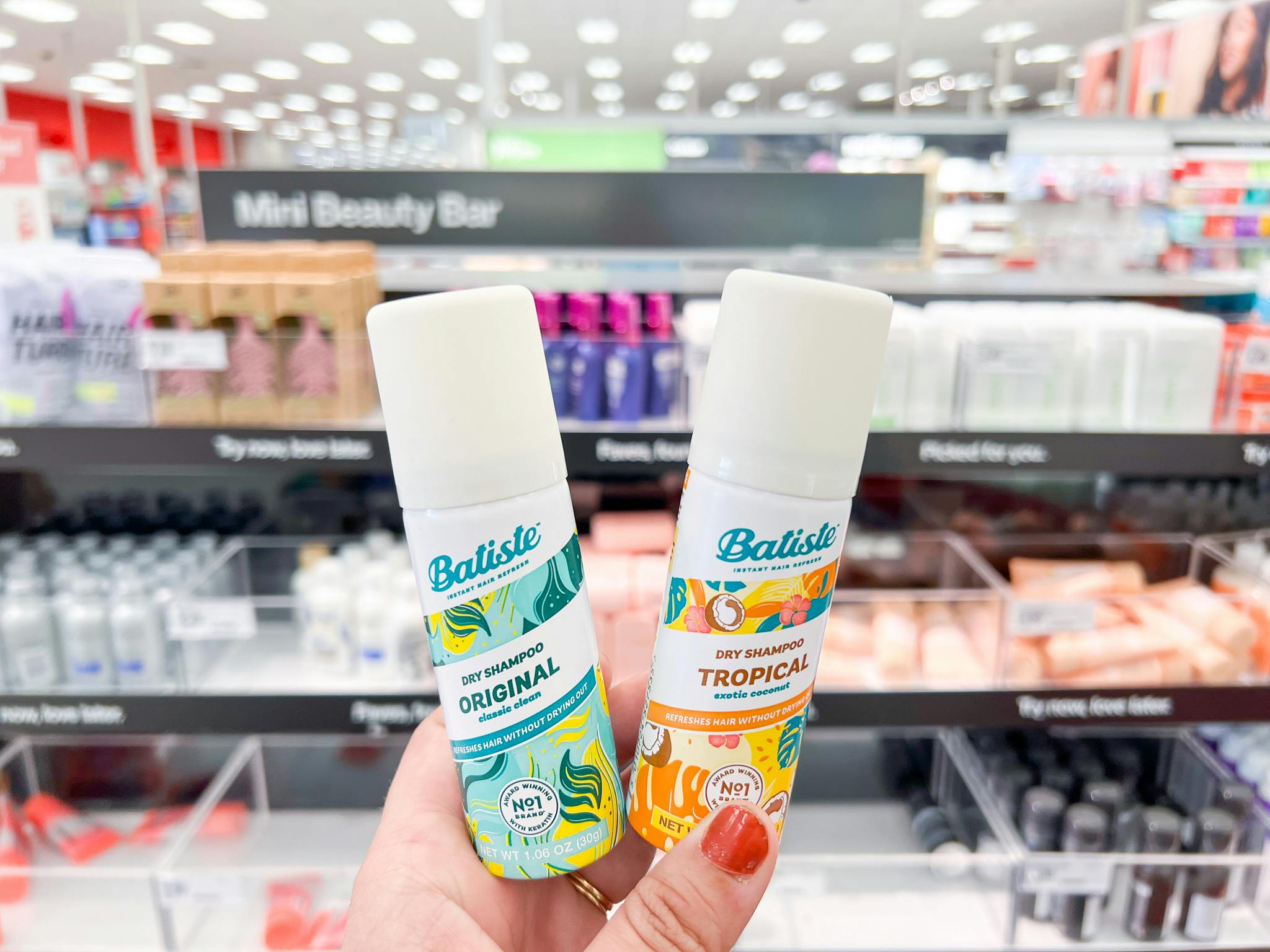 A hand holding two travel sized bottles of Batiste Dry Shampoo