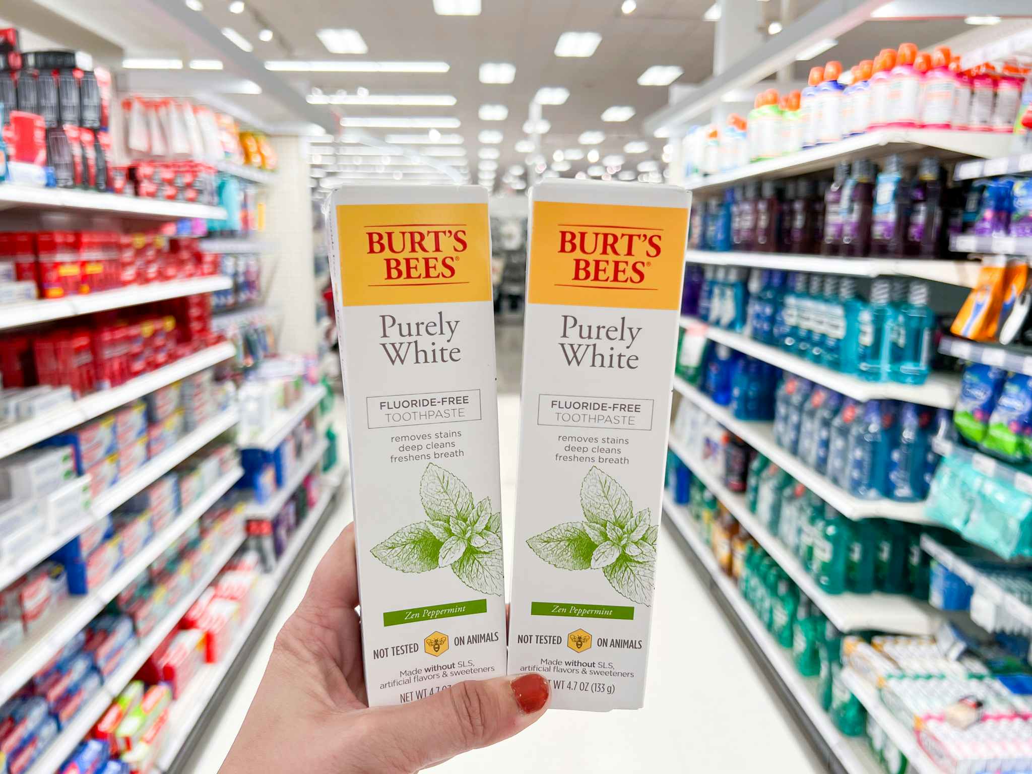 Two bottles of Burt's Bees purely white fluoride free toothpaste being held in the toothpaste aisle at Target