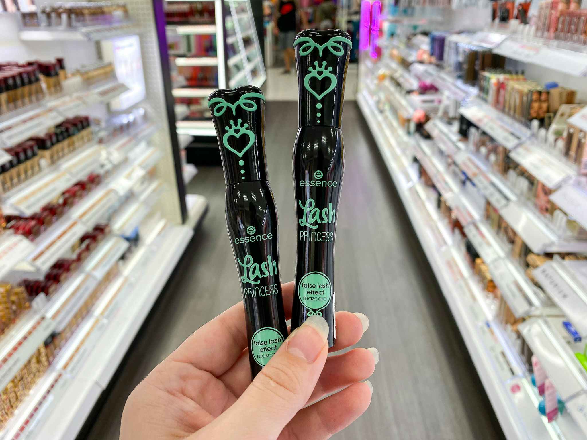 A person's hand holding up two essence Lash Princess False Lash Effect Mascaras in the beauty aisle at Target.