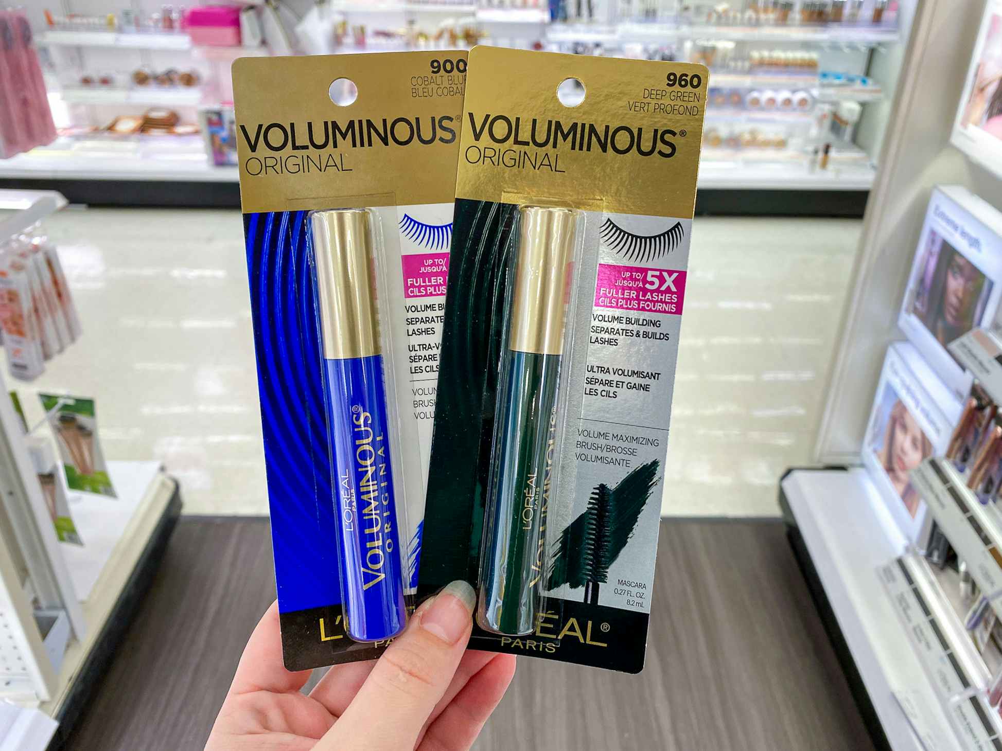 A person's hand holding up two different colors of L'Oreal Paris Voluminous Original Mascara in the beauty aisle at Target.