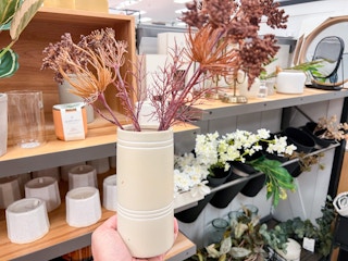 hand holding Heart and Hand vase and faux plants in front of other brand items