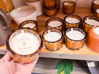 hand holding Hearth and Hand candle in front of shelf holding same candles
