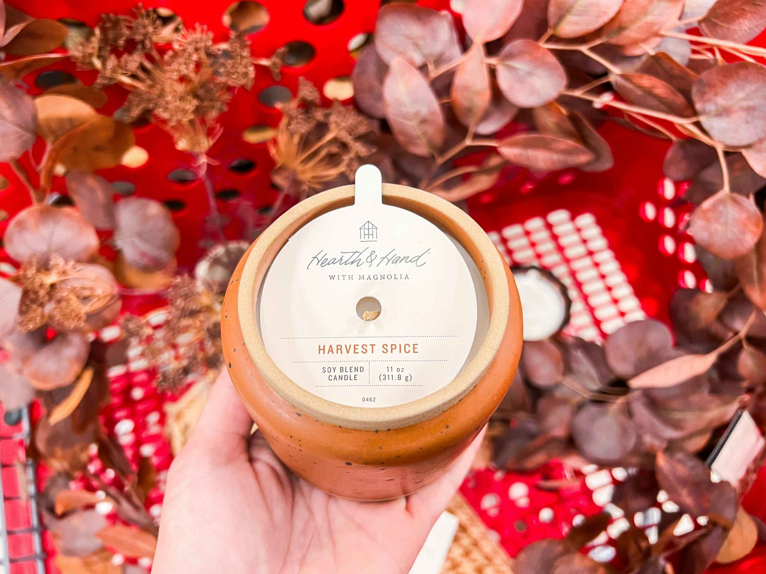 hand holding Hearth and Hand candle over other fall collection items in Target cart