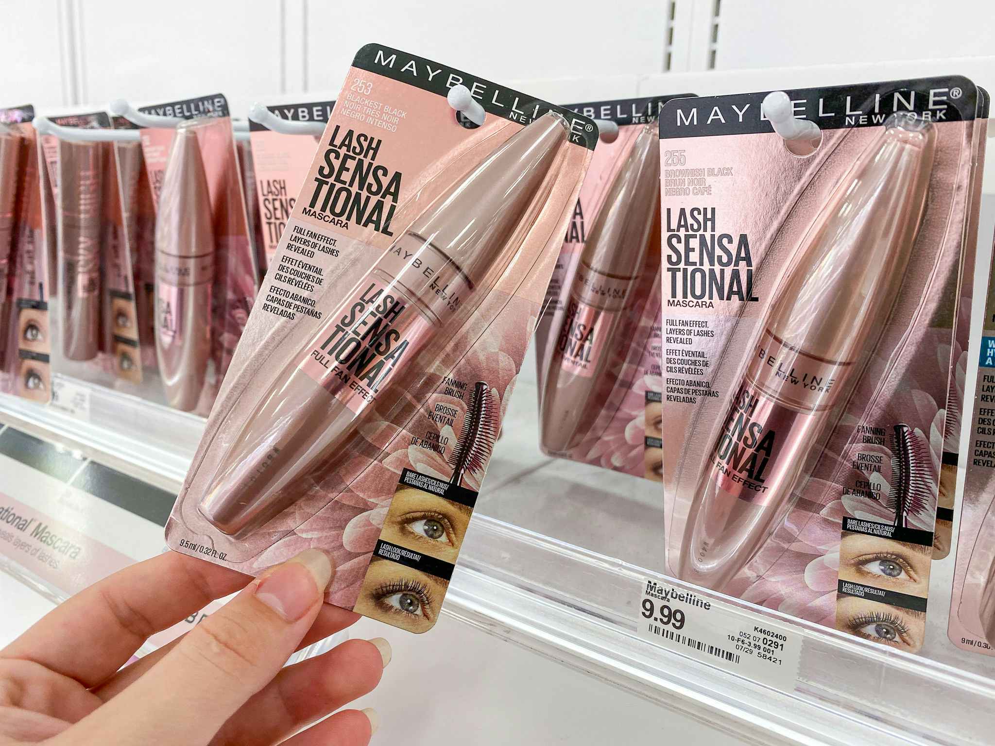 A person's hand reaching to take a Maybelline Lash Sensational Lengthening Mascara from the display in the beauty aisle at Target.