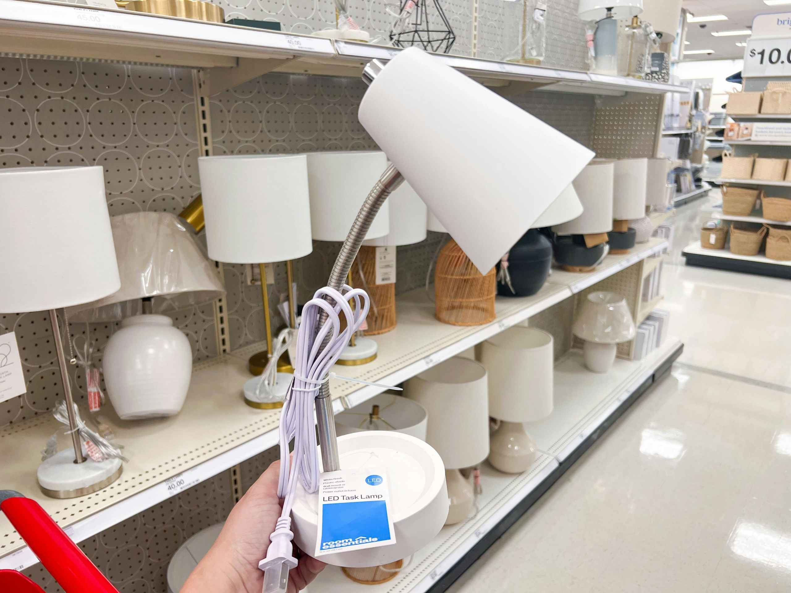 hand hold white Room Essentials task table lamp in front of Target shelf