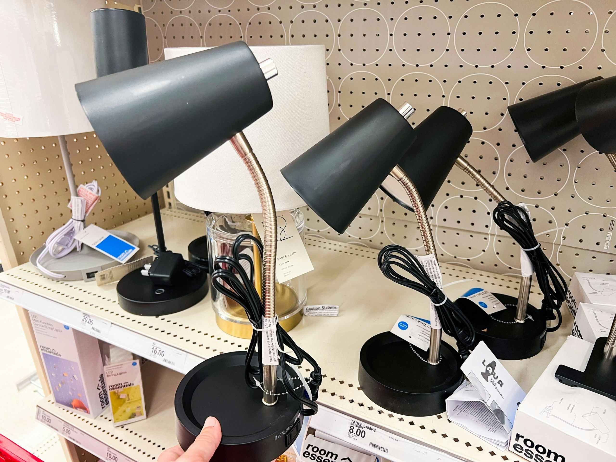 hand hold black Room Essentials task table lamp in front of Target shelf with like items