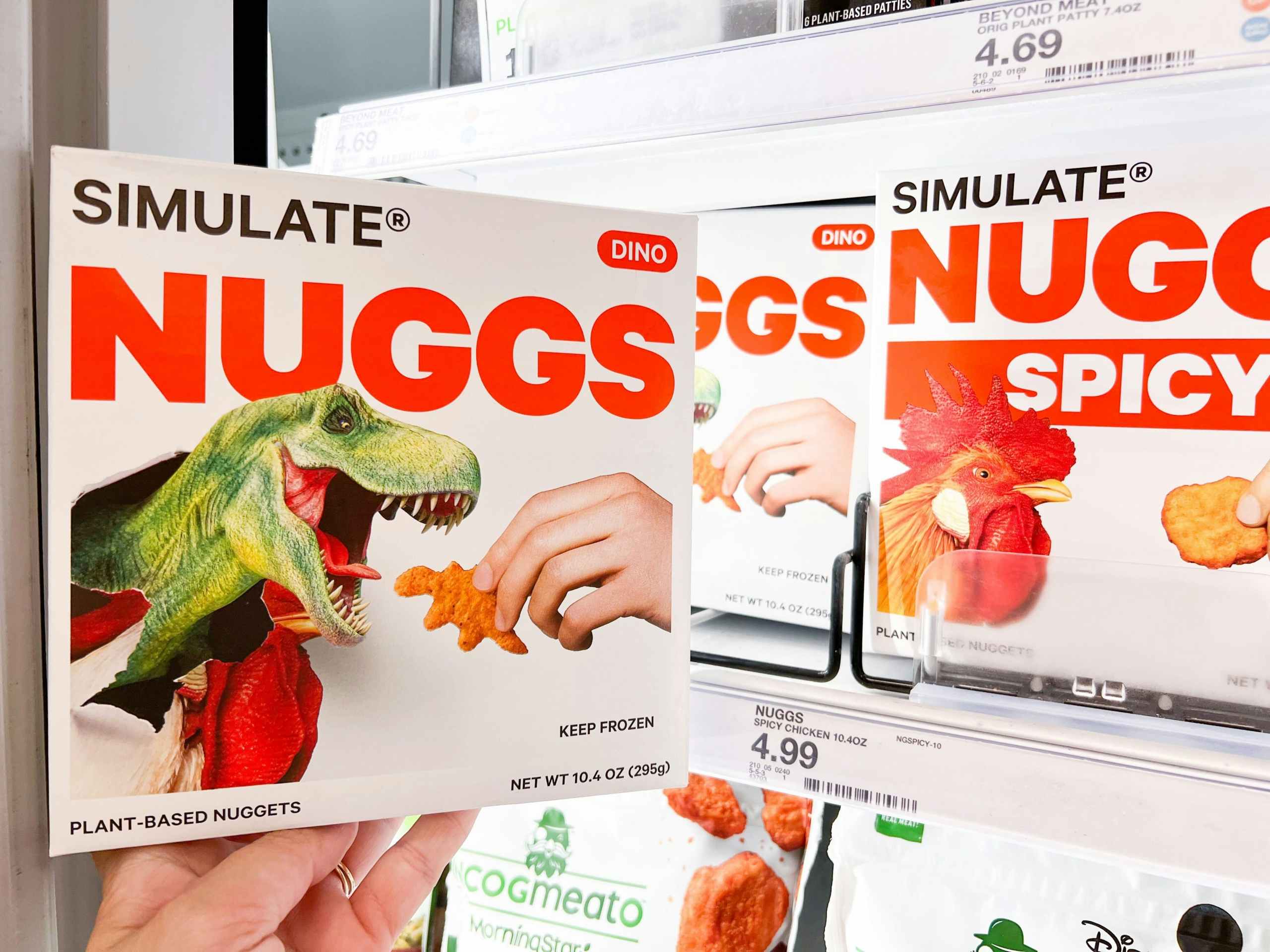 hand holding a box of Simulate Nuggs Dinos in front of like items in a Target storage freezer