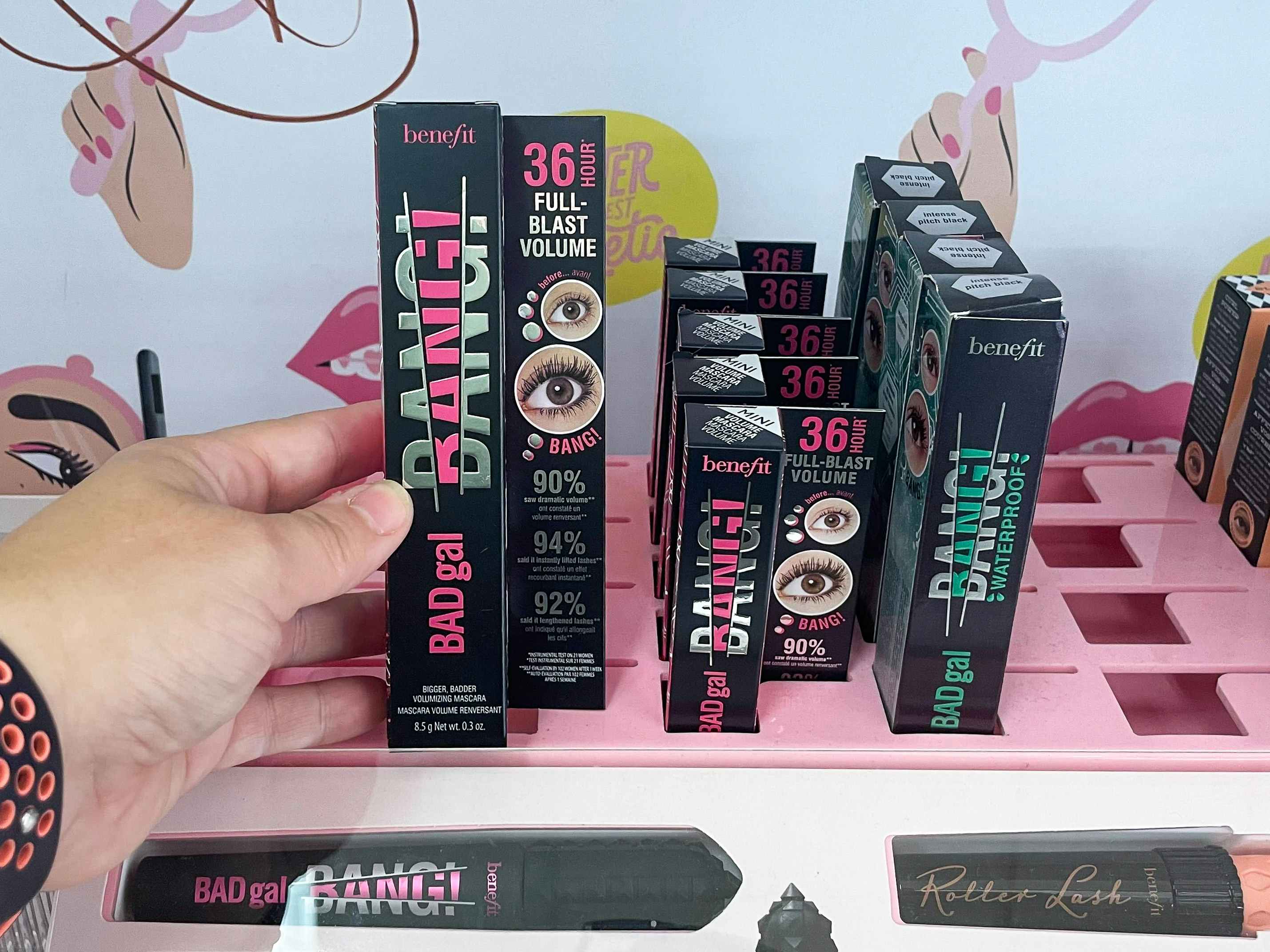 A person's hand reaching to take a Benefit Cosmetics BADgal BANG! Volumizing Mascara from the shelf in Target.