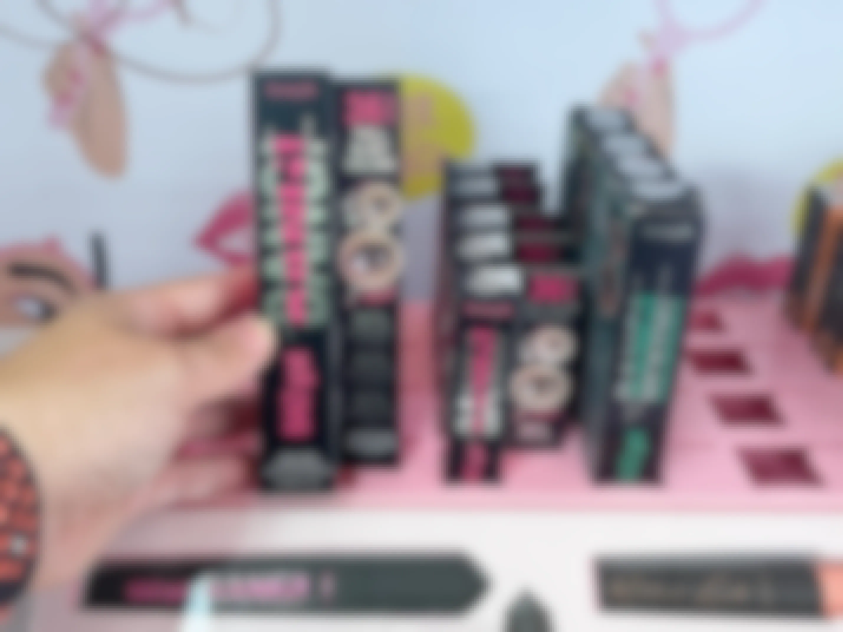 A person's hand reaching to take a Benefit Cosmetics BADgal BANG! Volumizing Mascara from the shelf in Target.