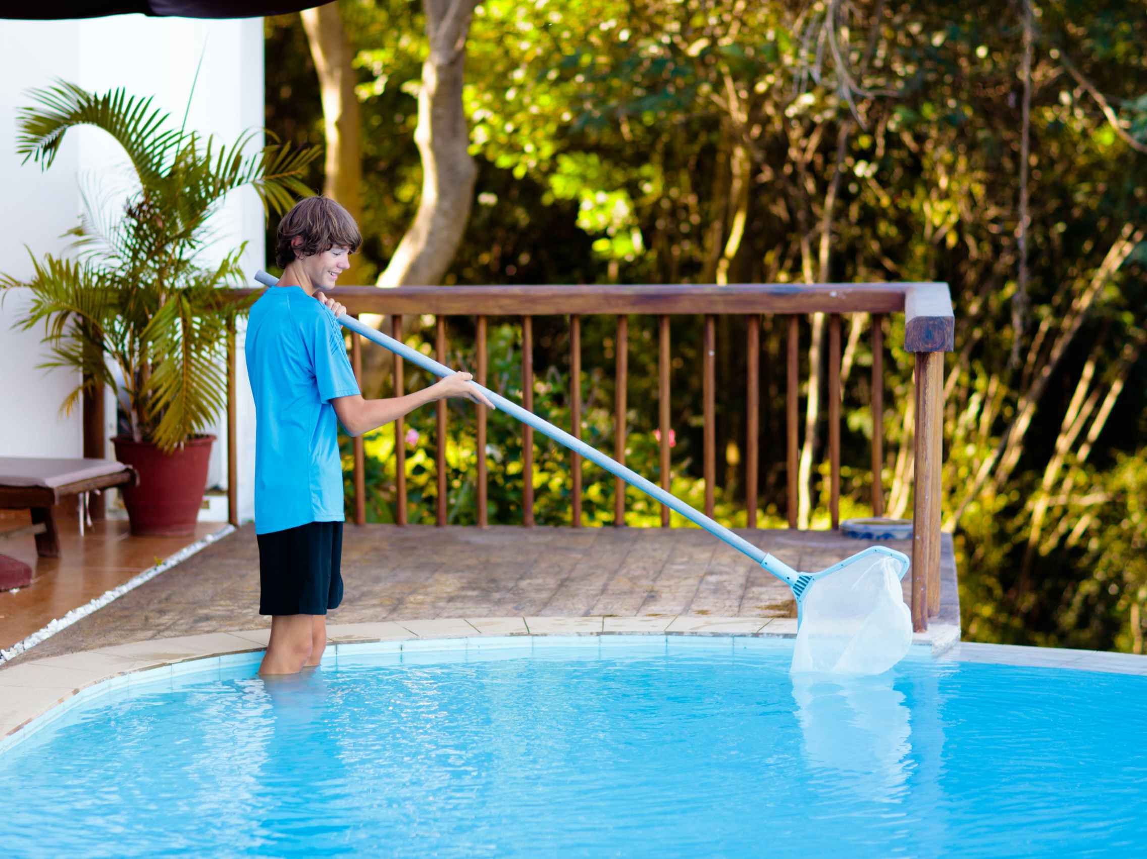 A teenage boy using a pool skimmer to clean debris from a pool.