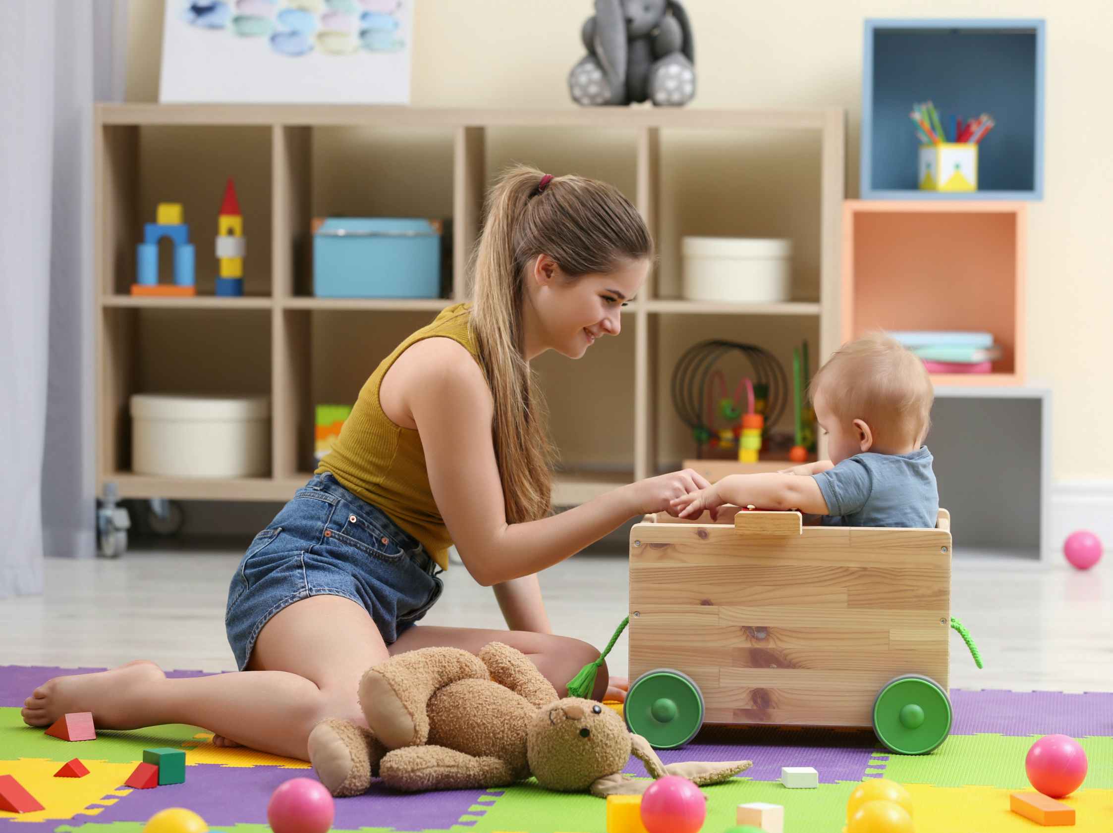 teenage girl child care worker playing with baby in playroom