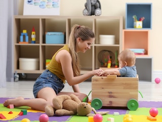 teenage girl babysitter playing with baby in playroom