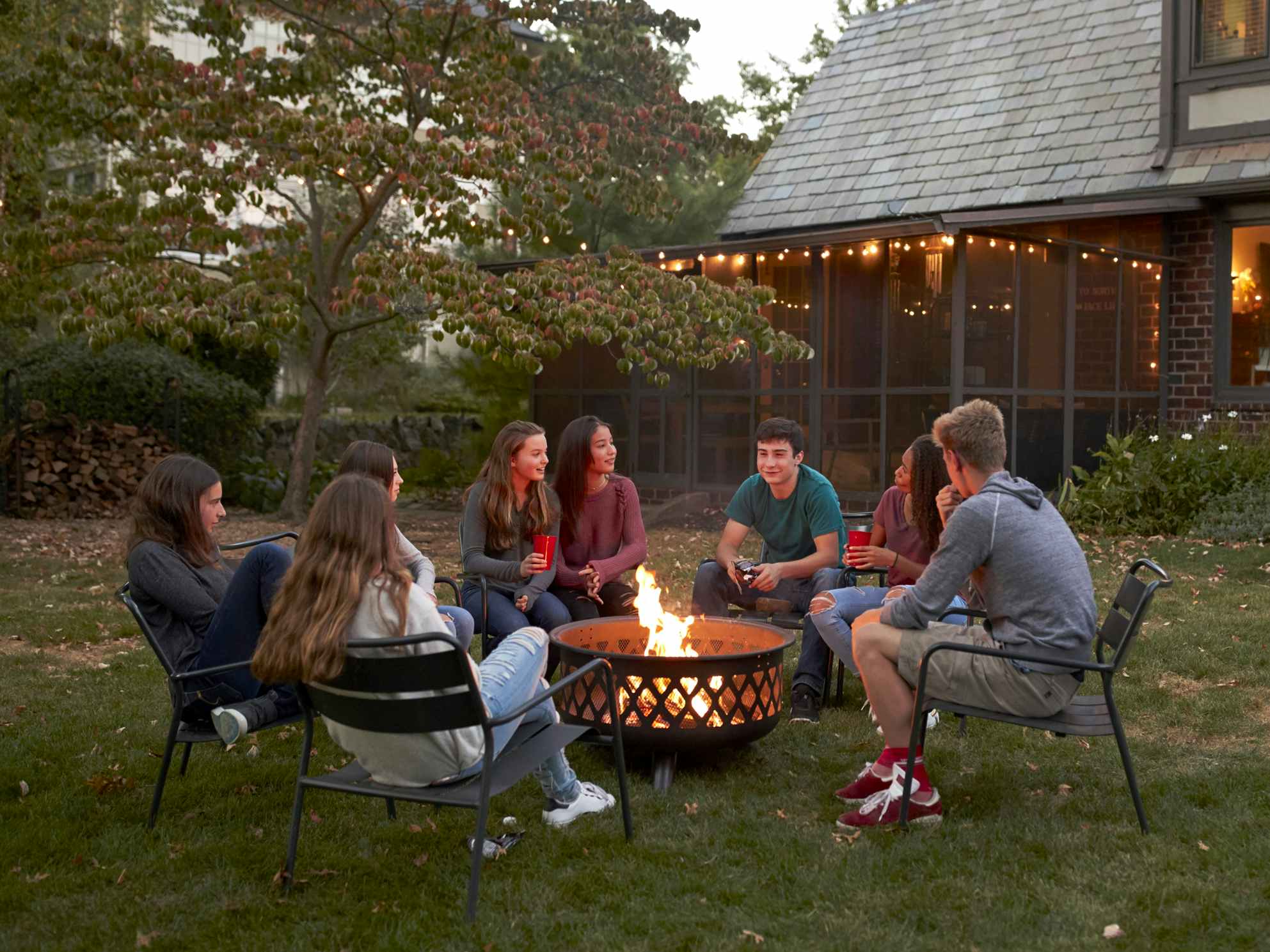 group of teenagers sitting around fire pit in autumn