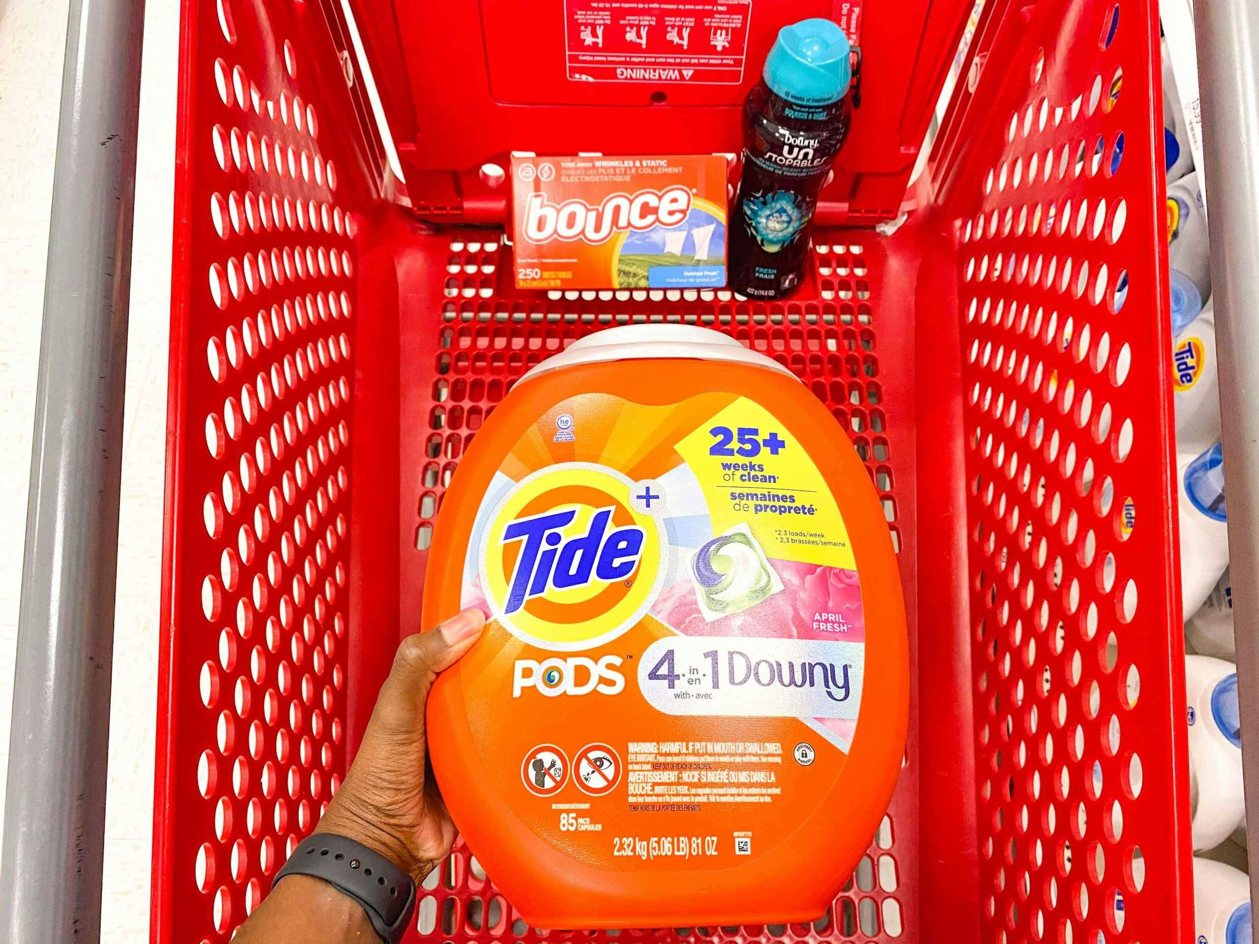 hand holding Tide Pods, bounce dryer sheets, downy unstopables together in a Target shopping cart