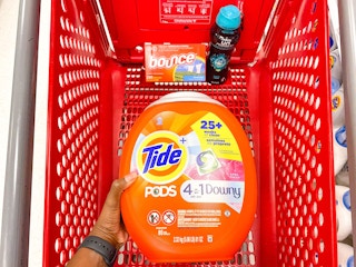 hand holding Tide Pods, bounce dryer sheets, downy unstopables together in a Target shopping cart
