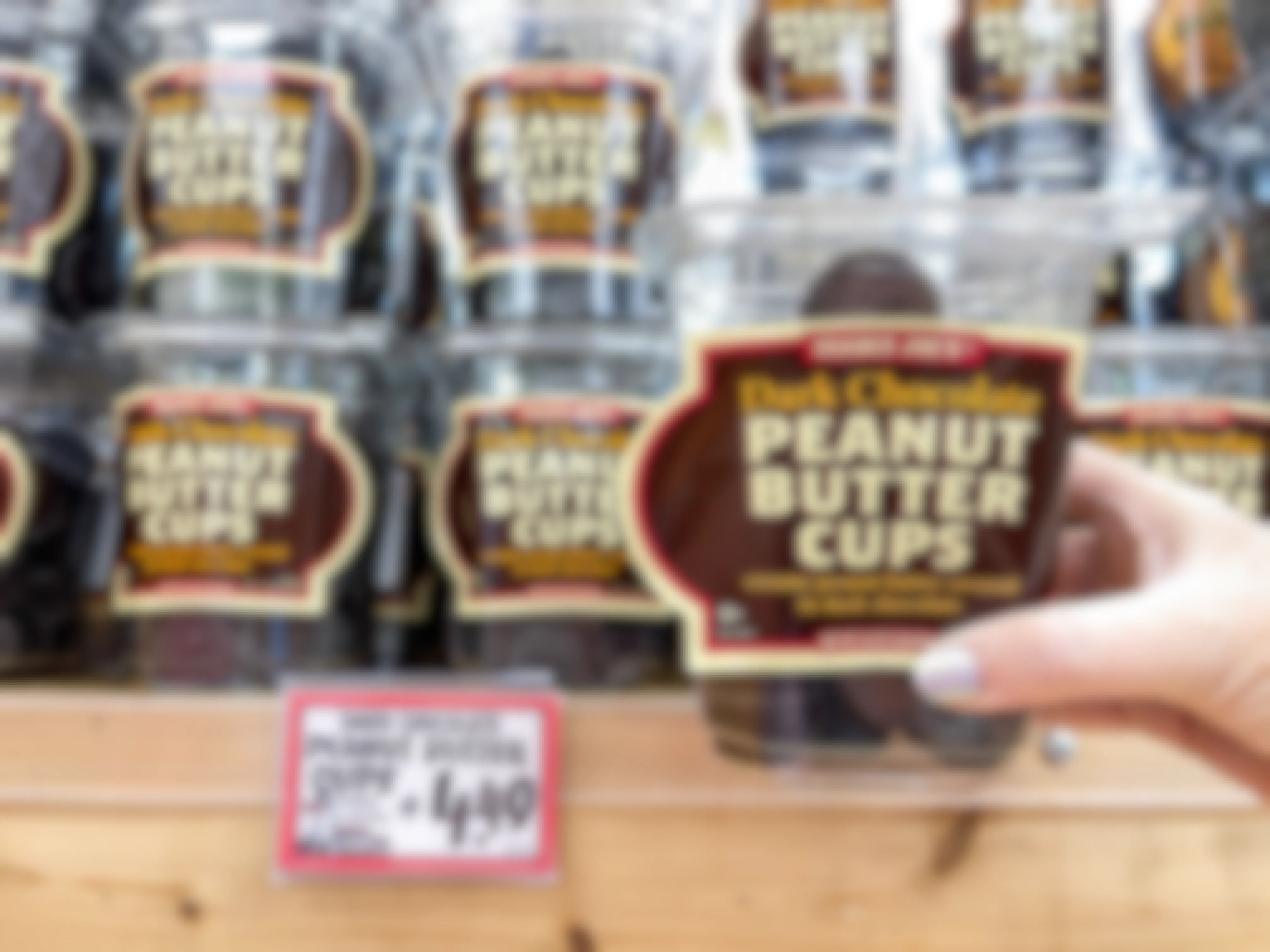 A person's hand holding a cup of Trader Joe's Dark Chocolate Peanut Butter Cups in front of a display of them on a shelf at Trader Joe's.