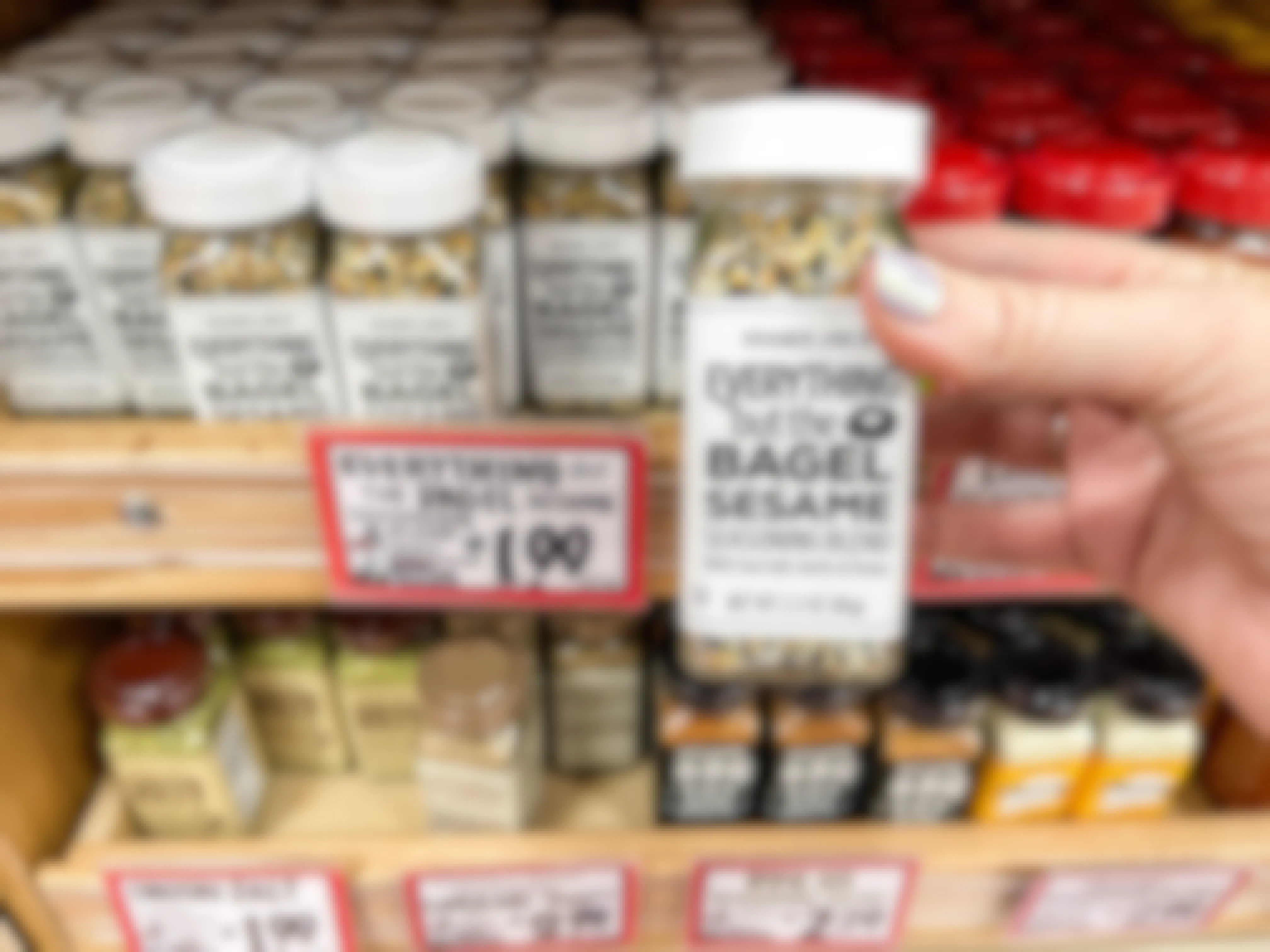 A person holding a container of Trader Joe's Everything but the Bagel Sesame Seasoning Blend in front of the seasonings shelf at Trader Joe's.